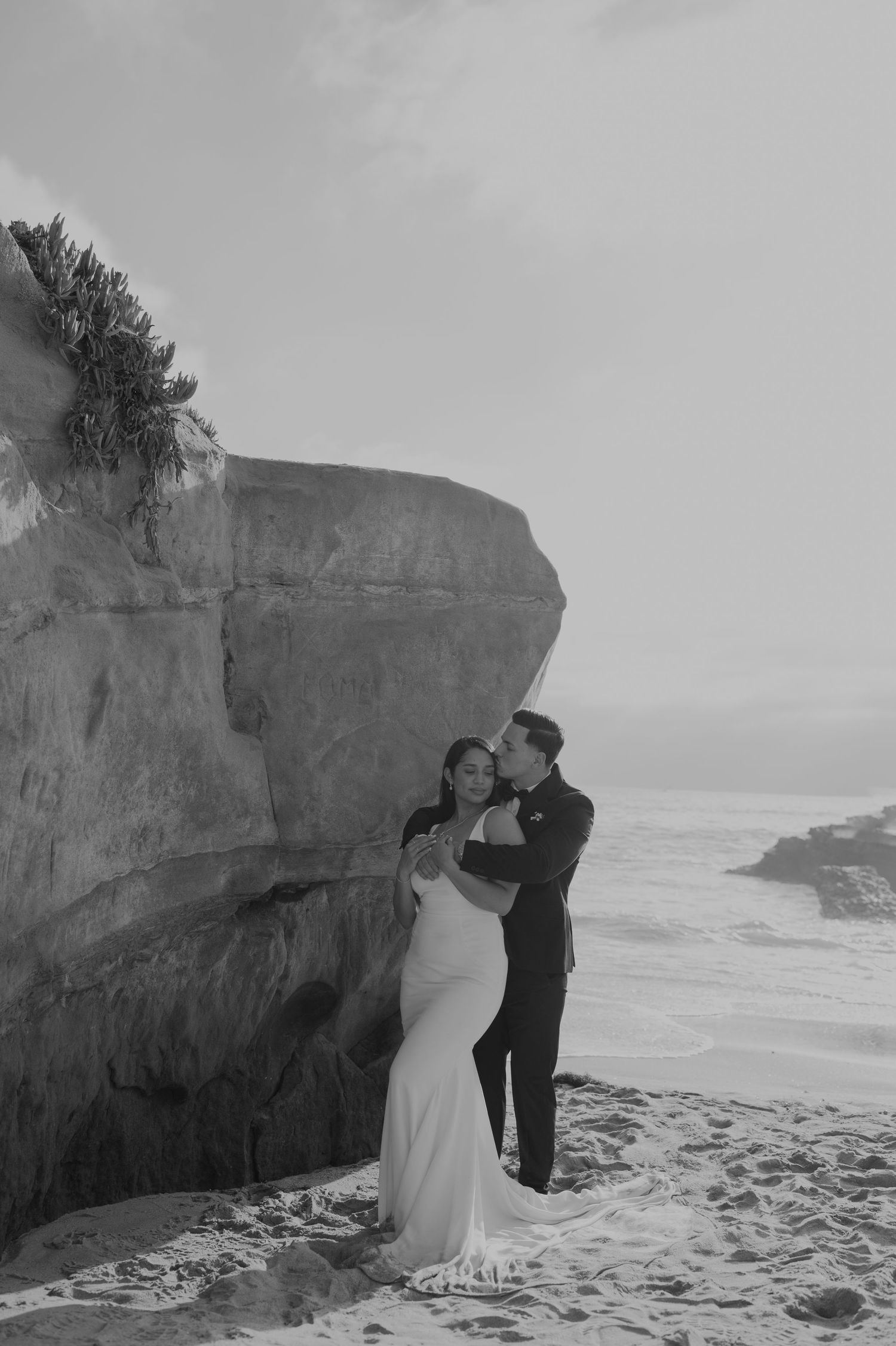 Black and white wedding portrait against dramatic coastal cliffs and crashing waves.