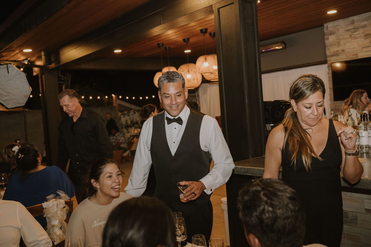 Elegantly dressed waiter in bow tie serving guests at an upscale indoor wedding reception dinner.
