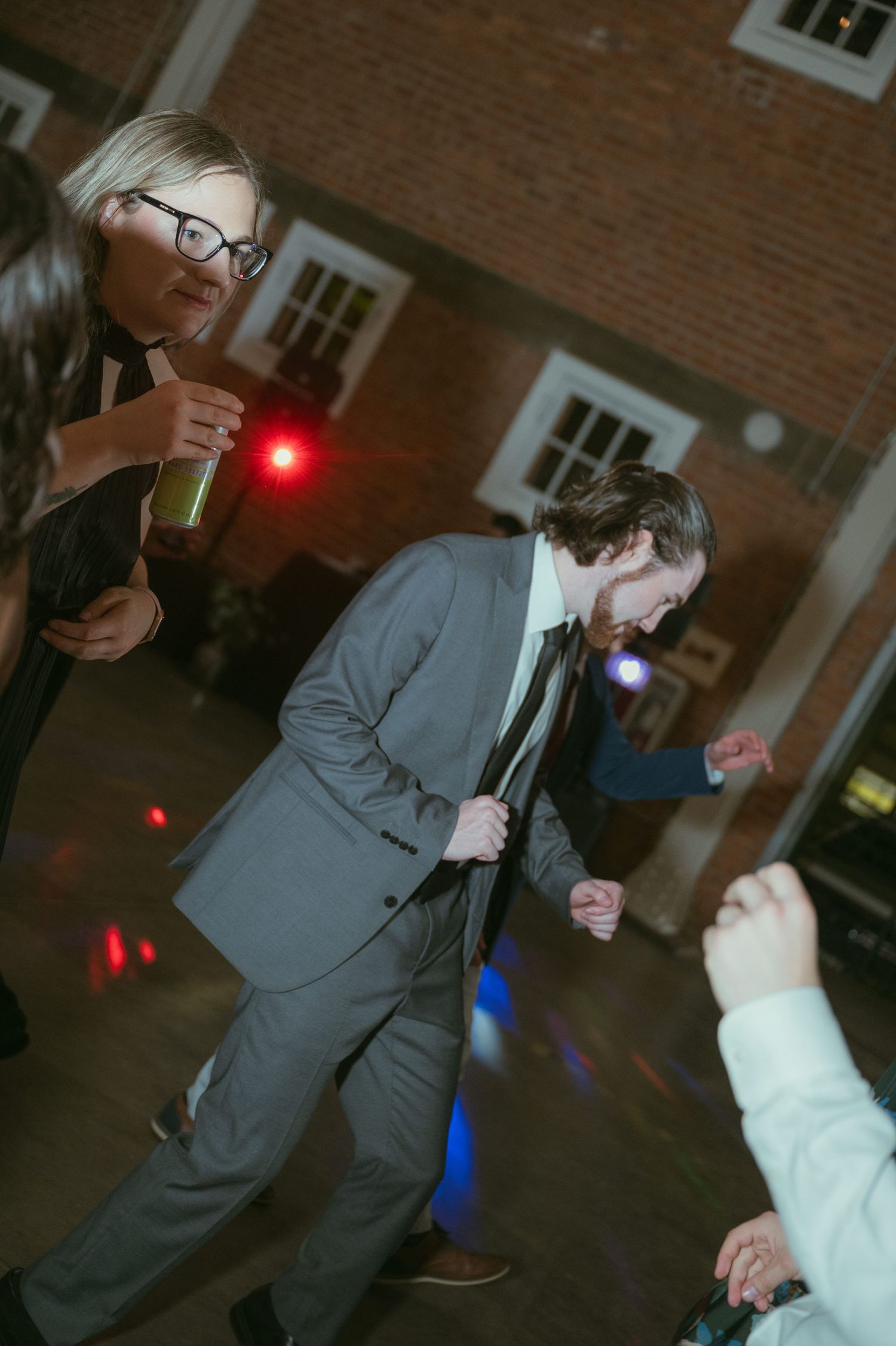 Guest in gray suit energetically dancing at a lively wedding reception with colorful DJ lights.