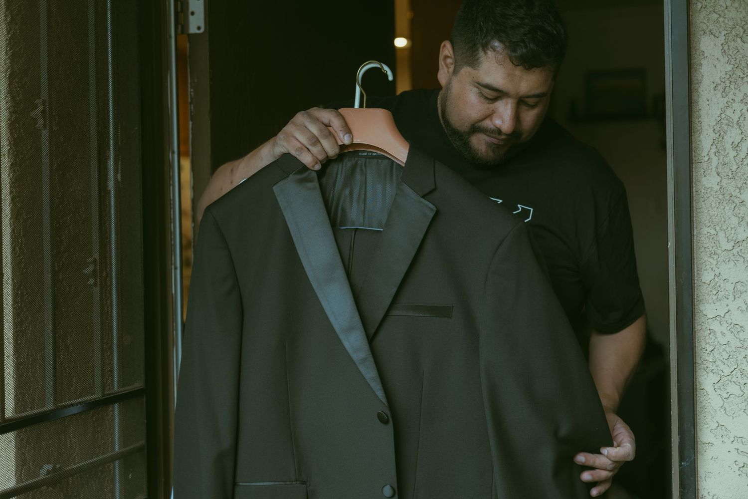 Man holding a dark suit jacket on a hanger in a doorway, preparing formal attire.