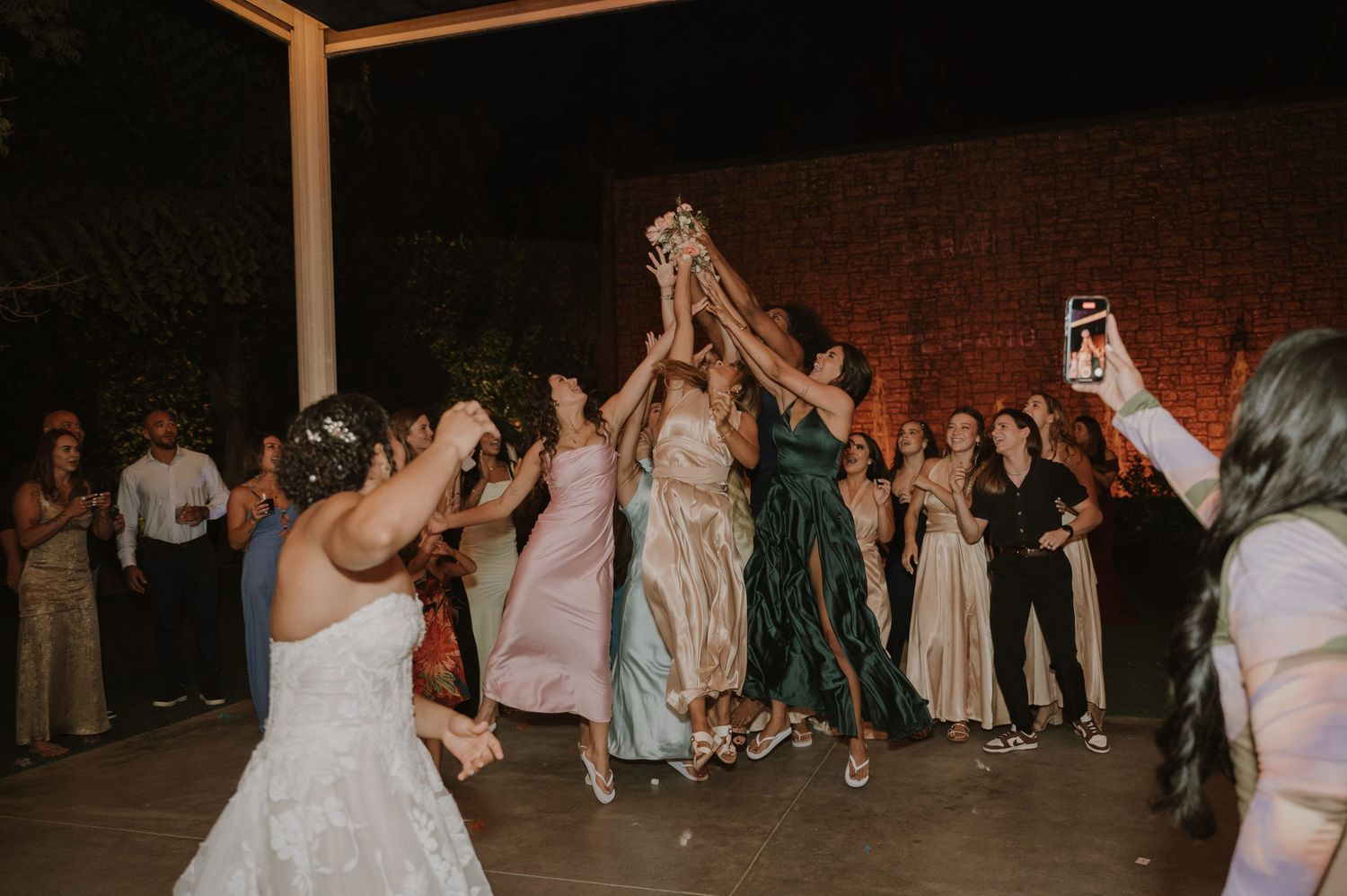 A bride tosses her bouquet to a group of excited women reaching up to catch it at a wedding.