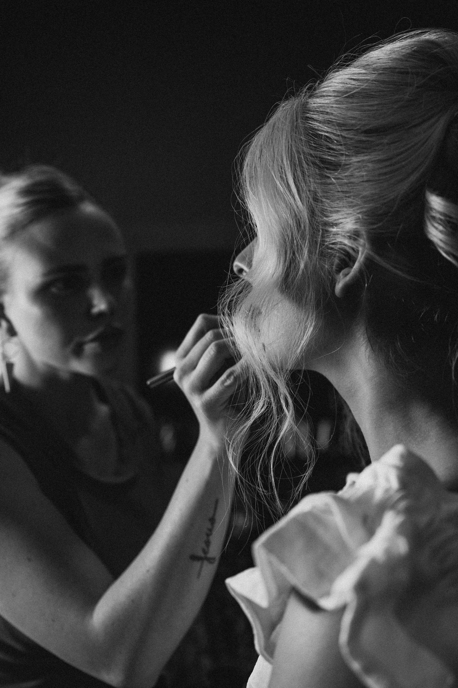 Black and white photo of a makeup artist applying makeup to a bride with an elegant updo hairstyle.