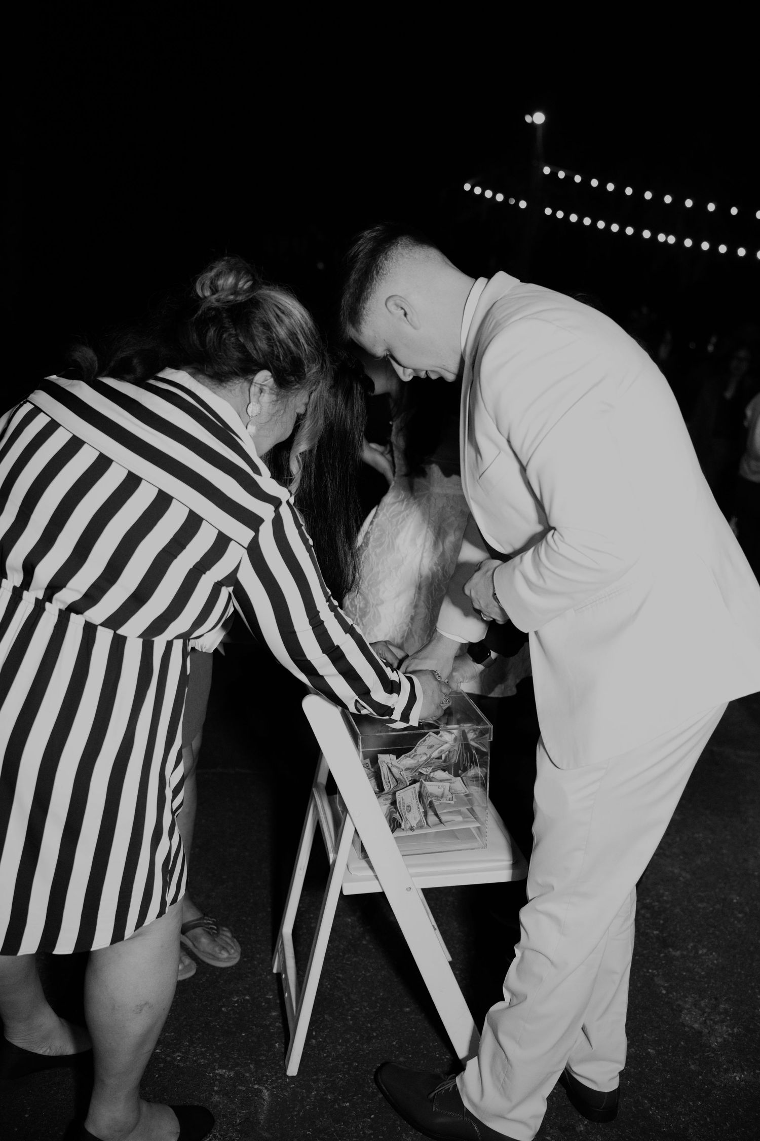 Black and white photo of wedding guests signing guestbook with bride and groom at nighttime reception.