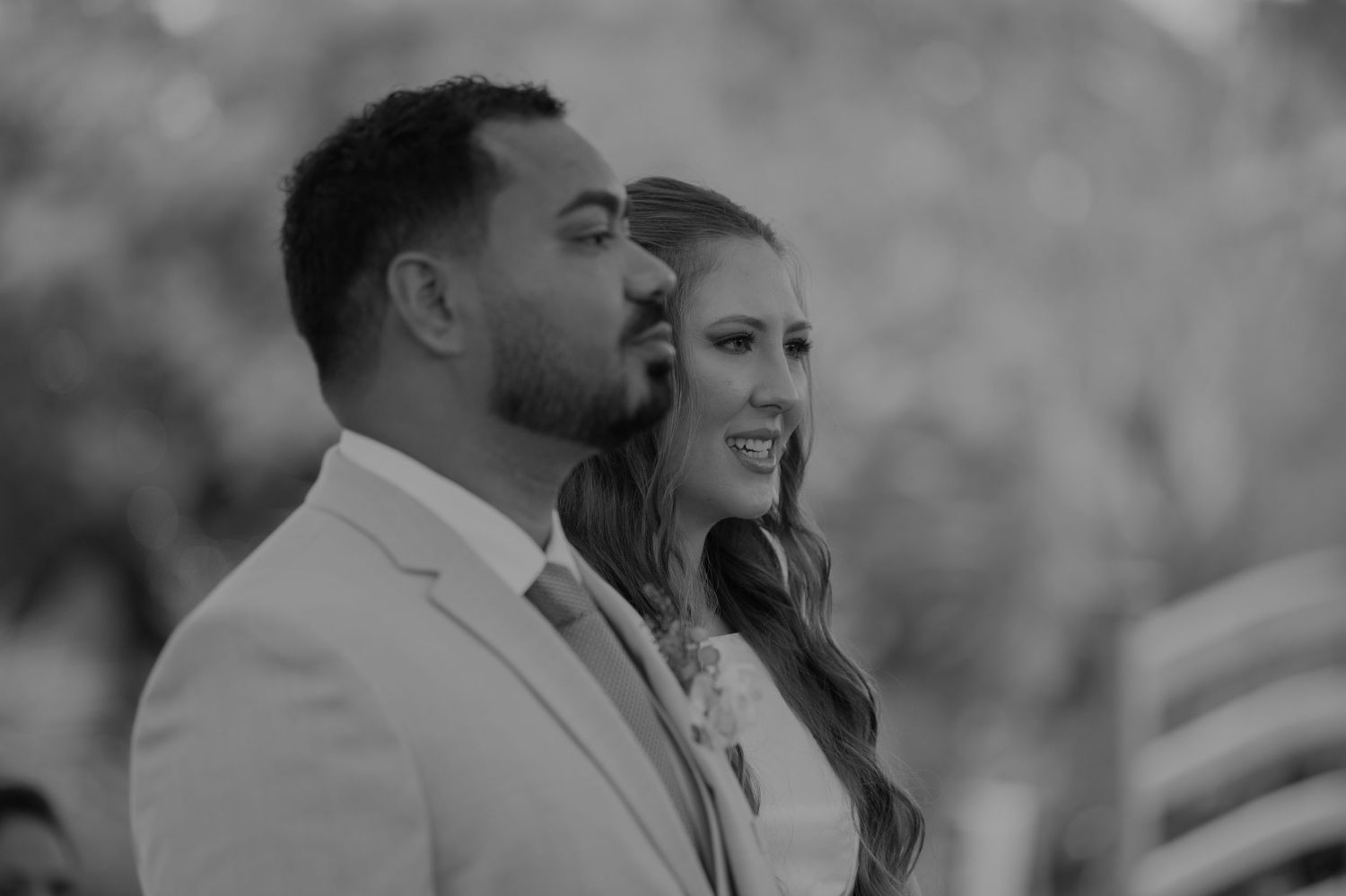 Black and white photo of a smiling bride and groom during their wedding ceremony outdoors.