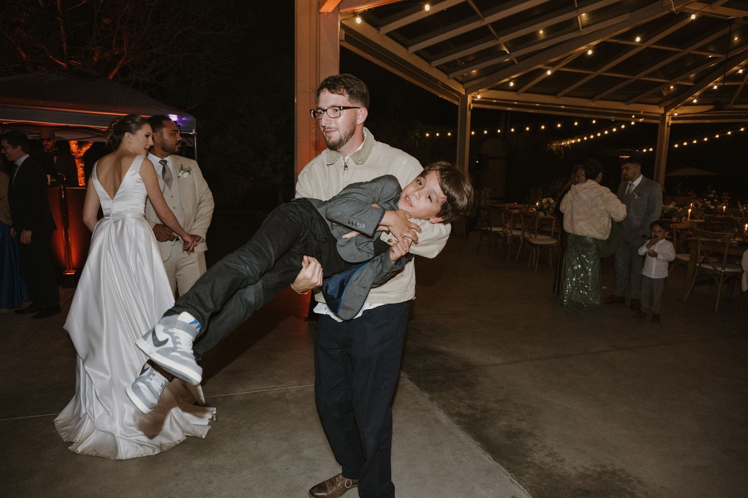 Groom carries a guest on the dance floor at a festive outdoor wedding reception.