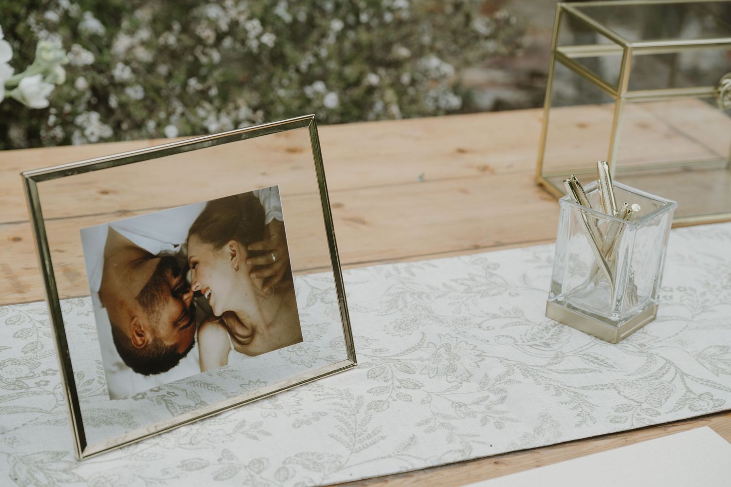 Gold-framed wedding photo display on linen table runner beside crystal pen holder at elegant reception.