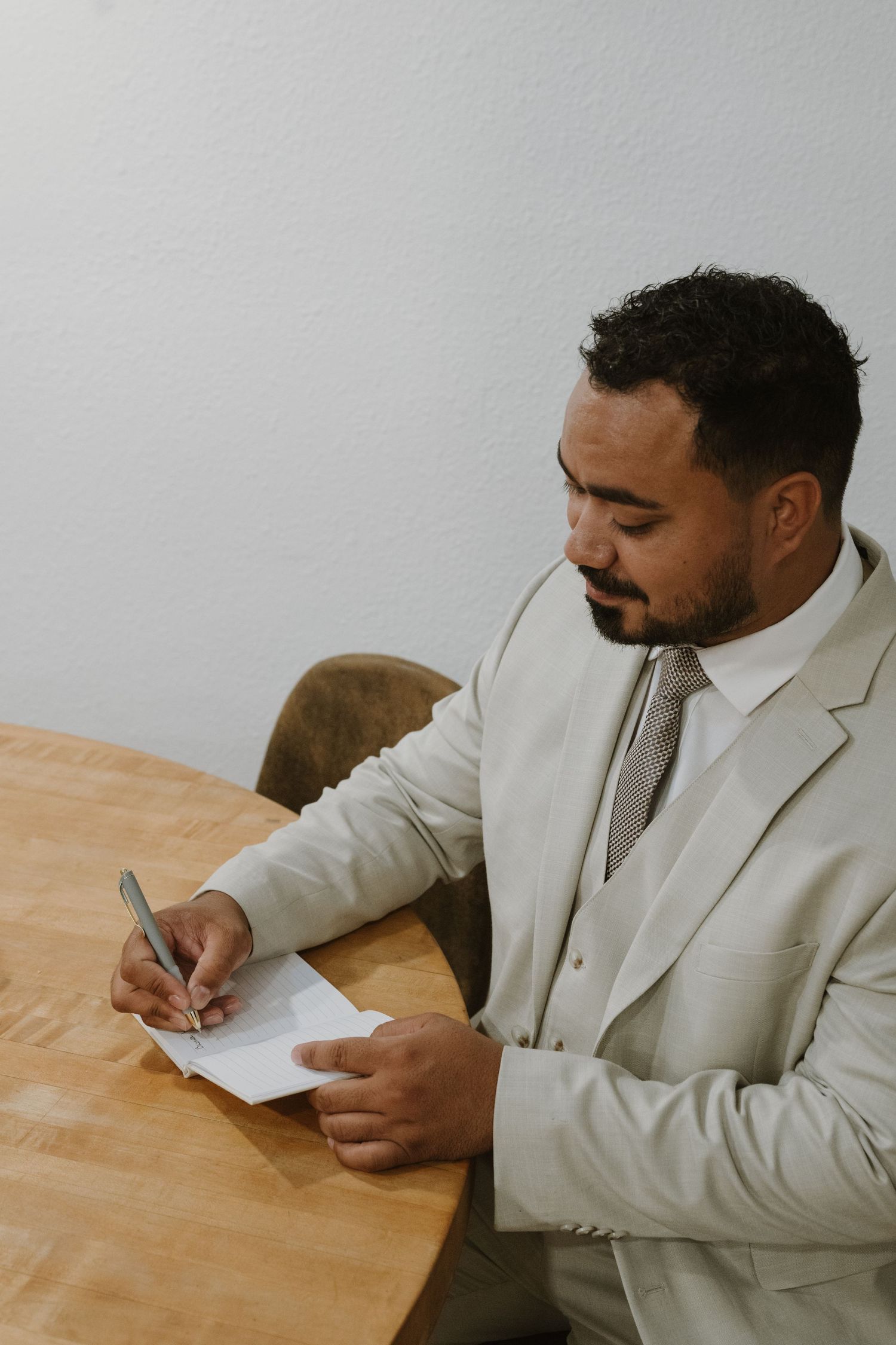 Professional man in light suit signing document at wooden table in office setting.