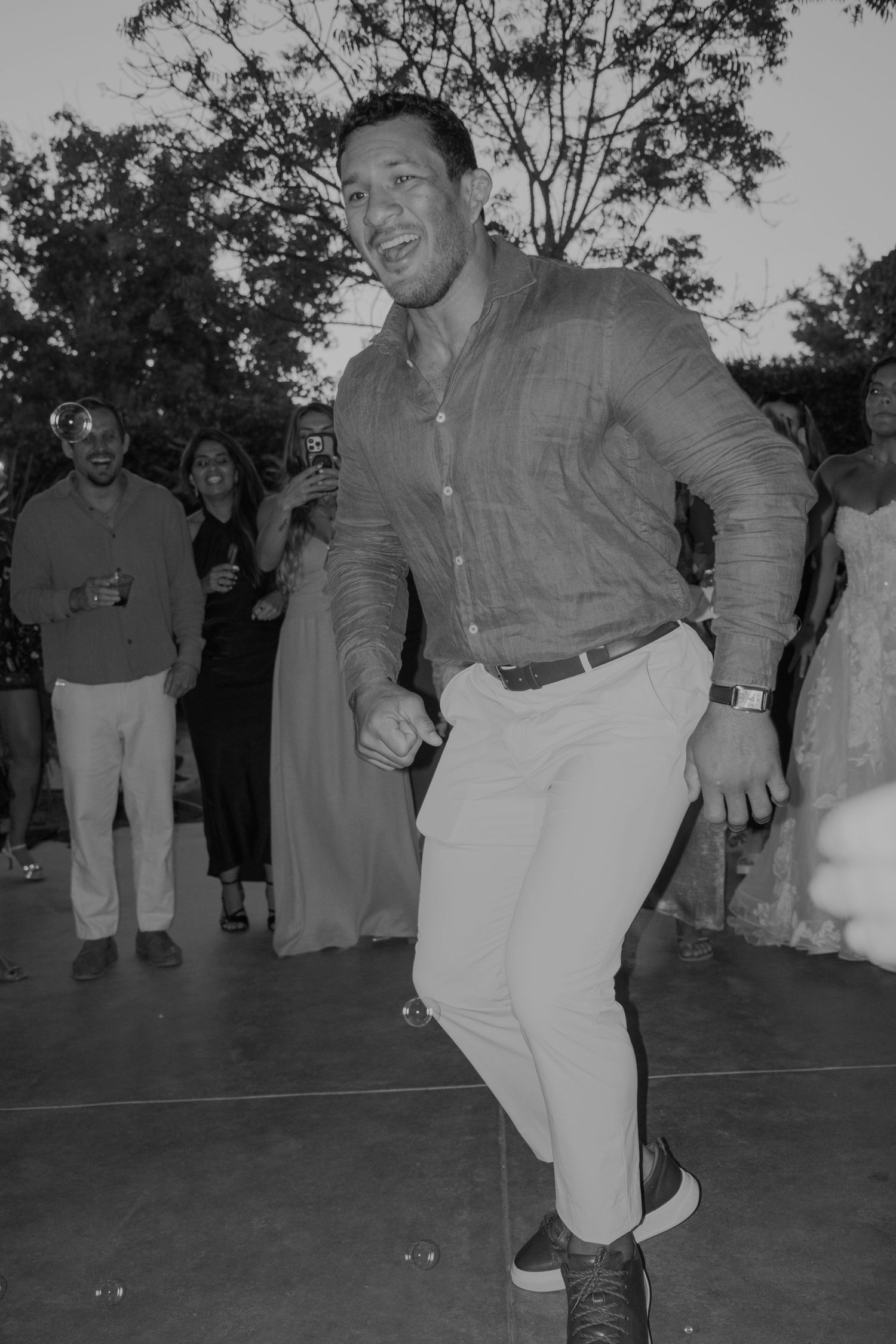 Man dancing energetically in black and white photo at outdoor wedding reception celebration.