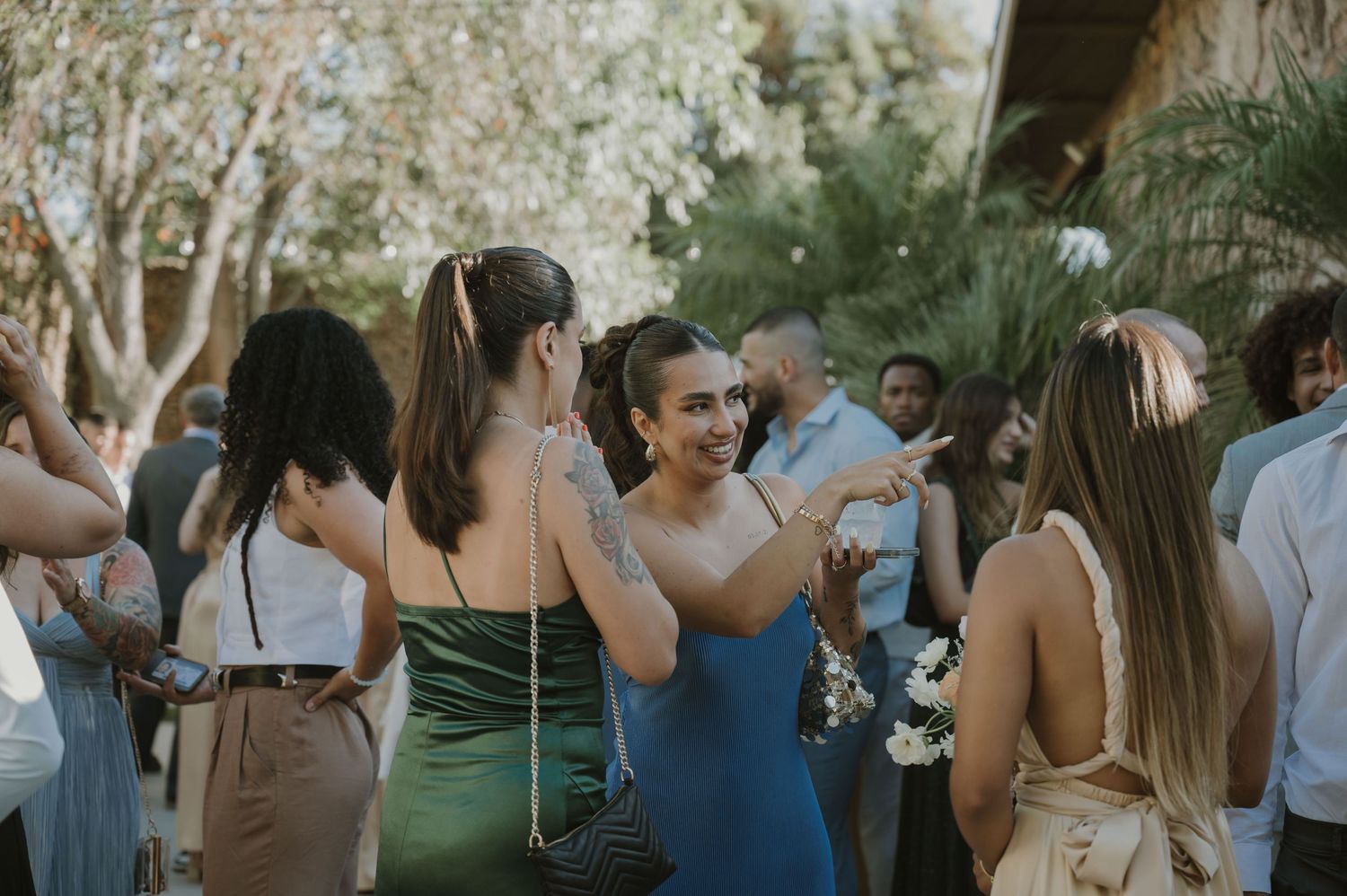 Women in elegant dresses socializing at an outdoor wedding reception party surrounded by lush greenery.