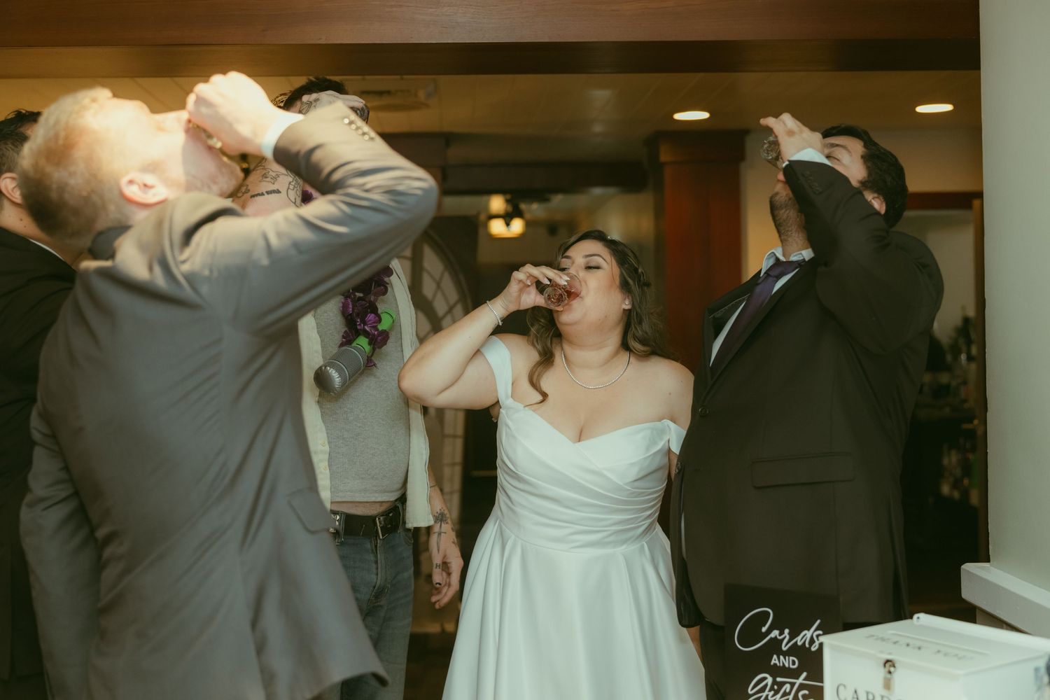 Bride in white gown does shots with guests during lively wedding reception celebration.