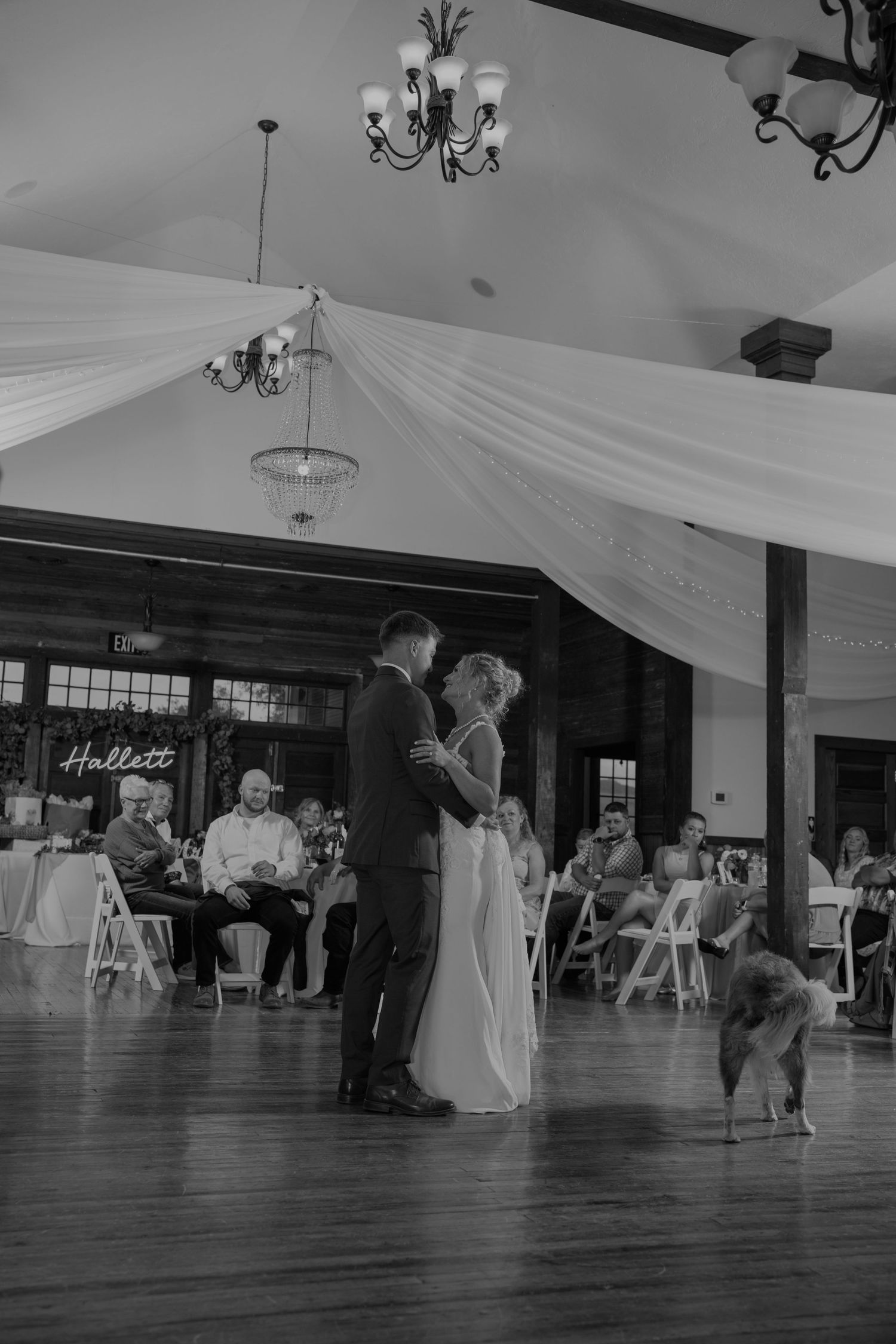 Black and white photo of wedding guests dancing in a rustic reception hall.