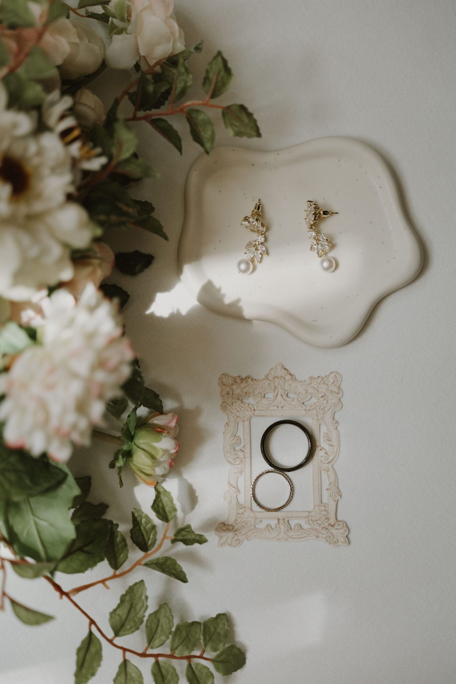 Wedding rings and delicate floral arrangements displayed on elegant white surfaces with ornate details.