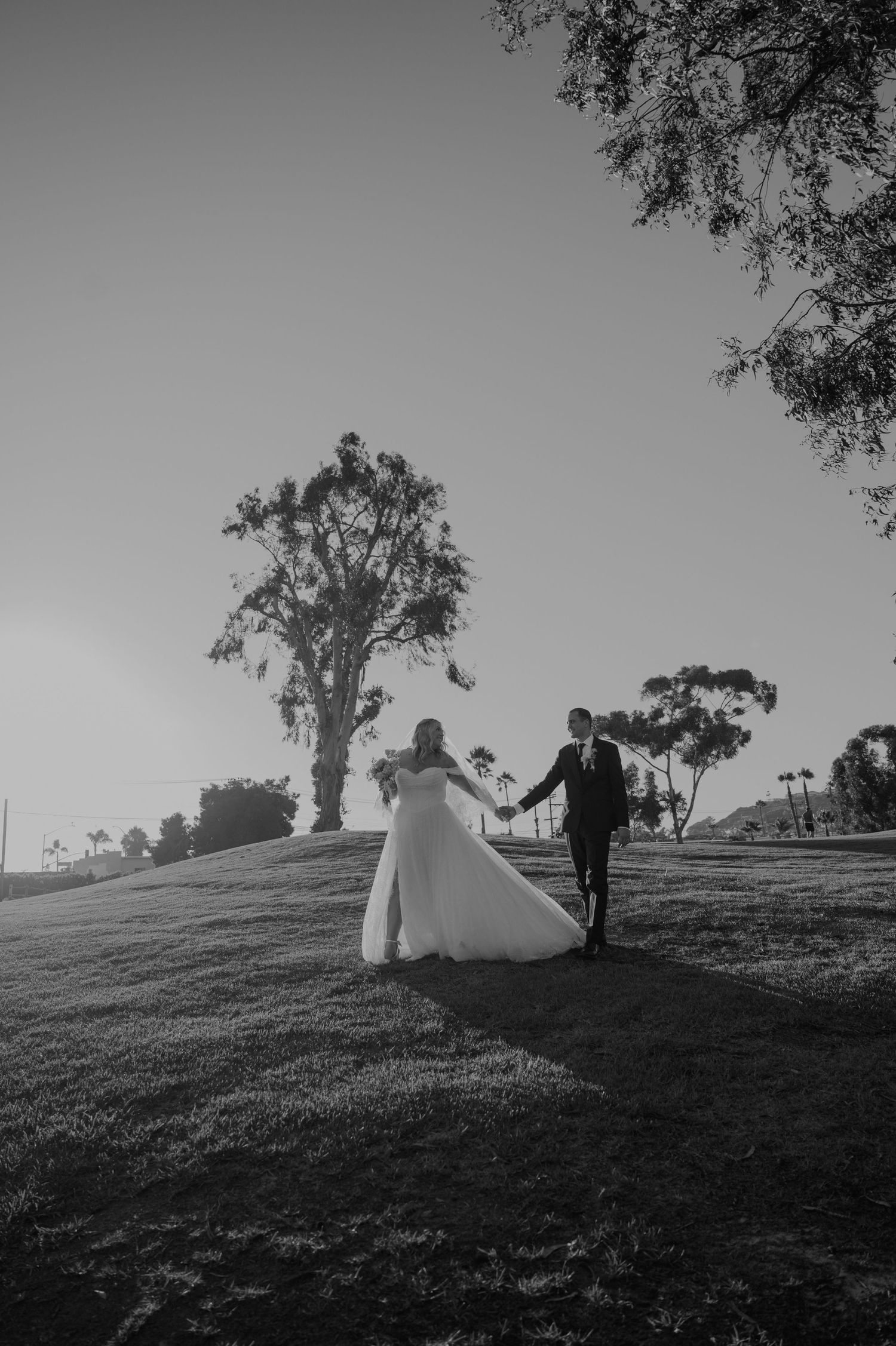 Black and white wedding photo of couple walking on hillside with trees.