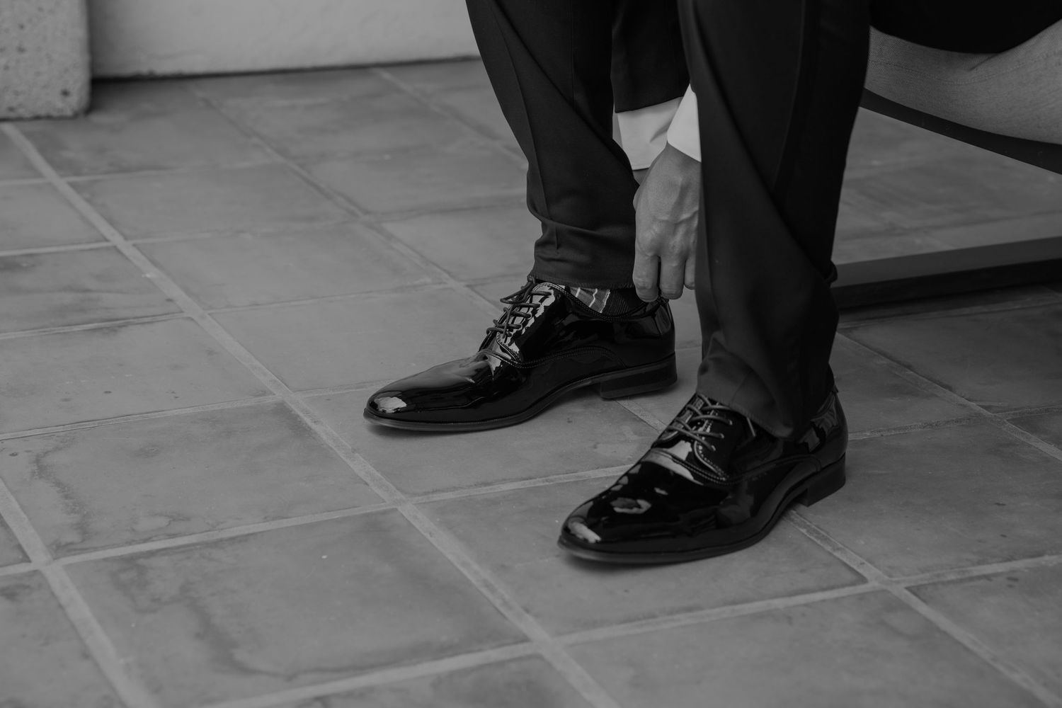 Multiple pairs of formal black shoes and dress pants shown from ankle level.