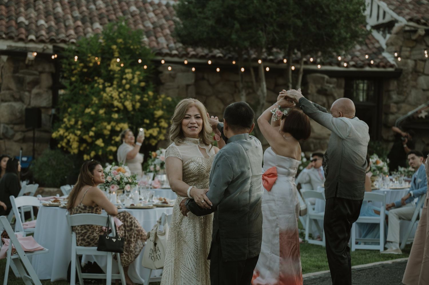 Guests dancing outdoors at an elegant wedding reception with string lights and floral centerpieces.
