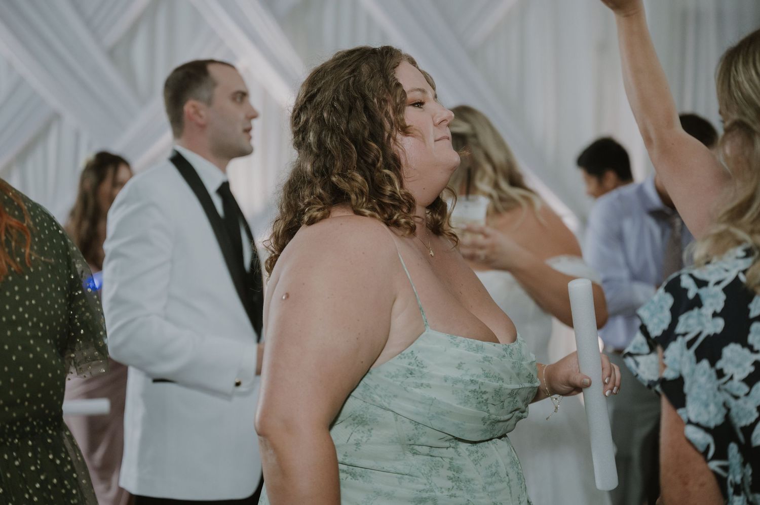 Wedding guest in green floral dress dancing joyfully at a wedding reception with draped white fabric backdrop.