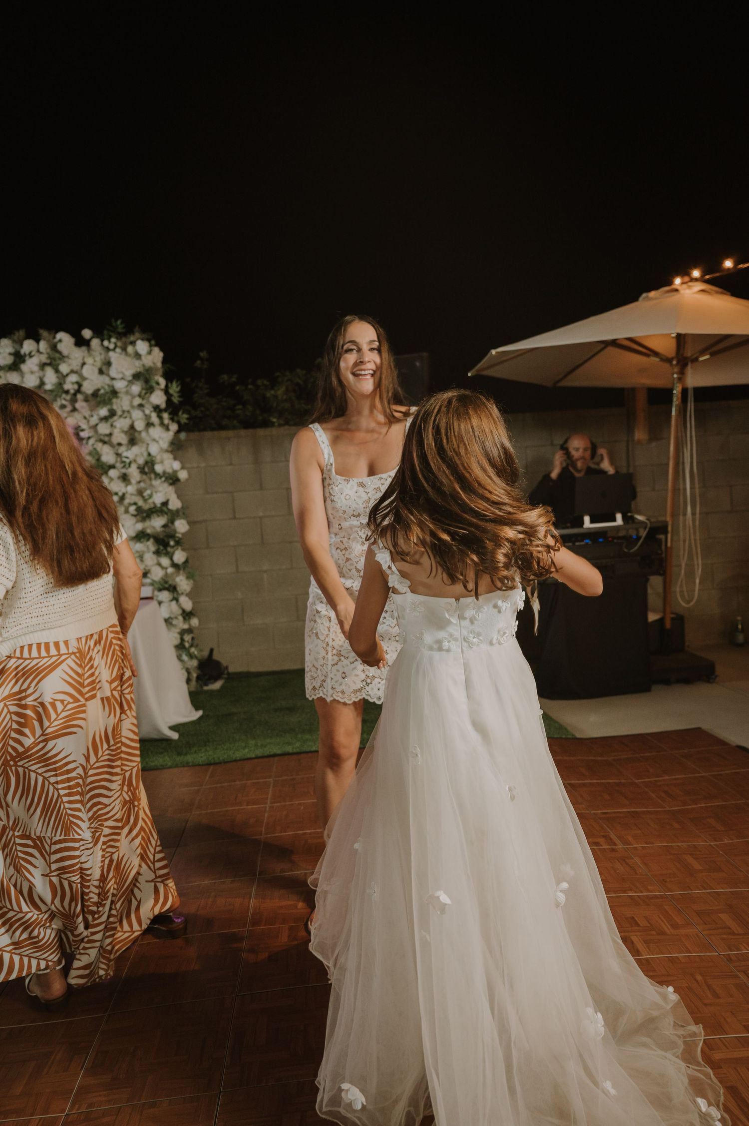 Bride in white tulle gown dancing with guest in lace dress at outdoor evening wedding reception.