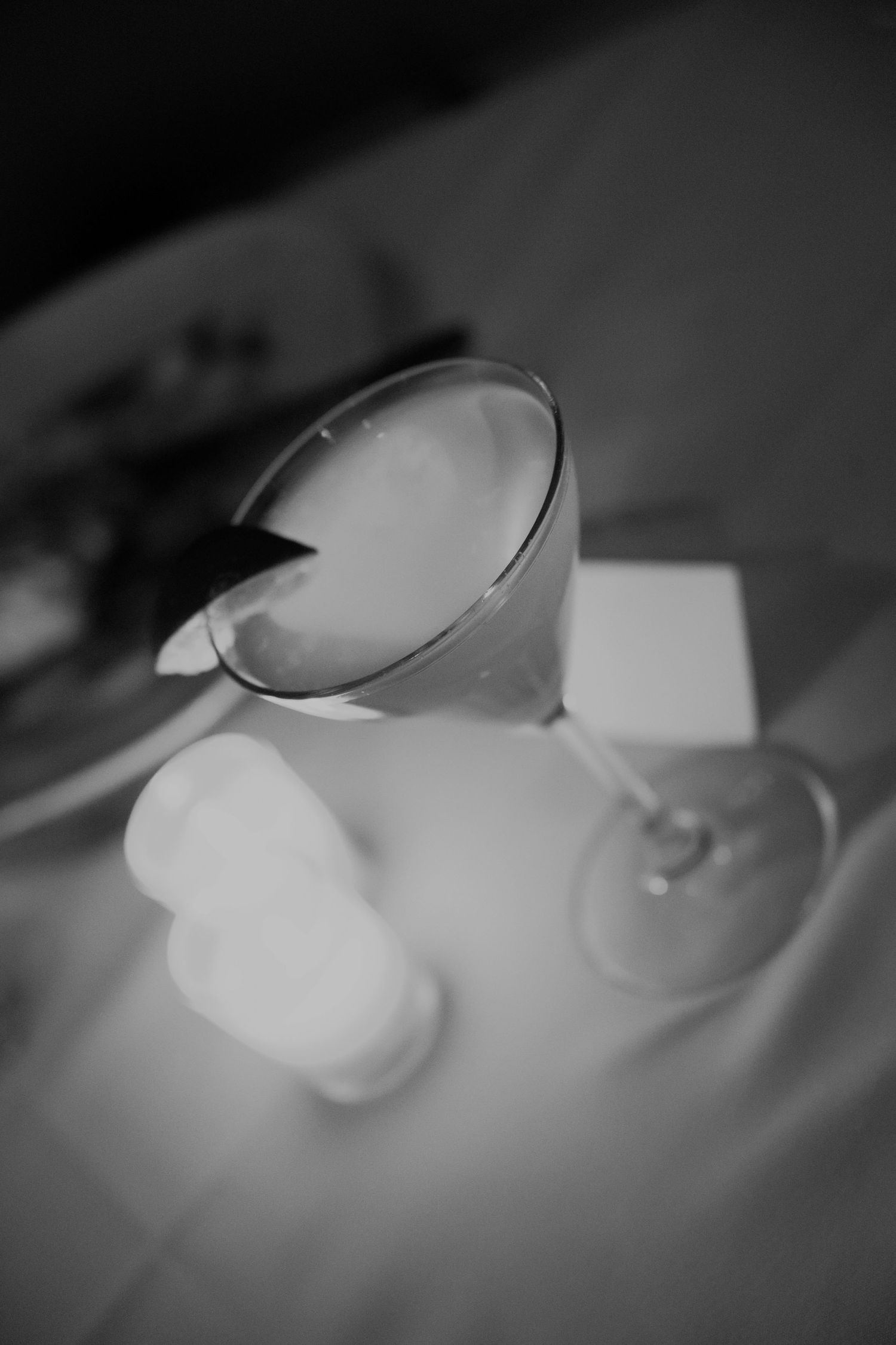 Black and white close-up of a martini cocktail glass on a white tablecloth at a wedding reception.