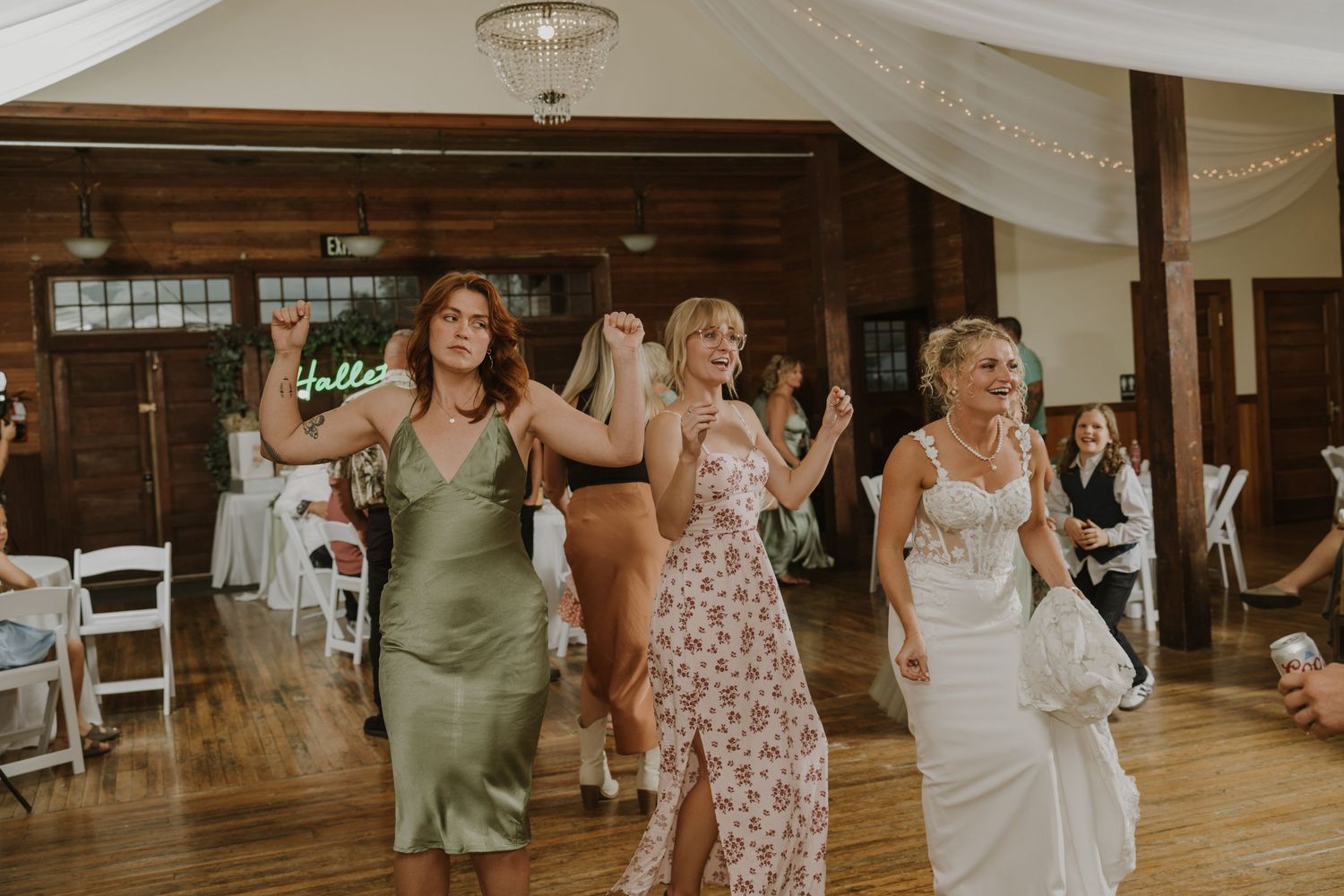 Wedding guests dancing and celebrating on a wooden dance floor at an indoor reception.