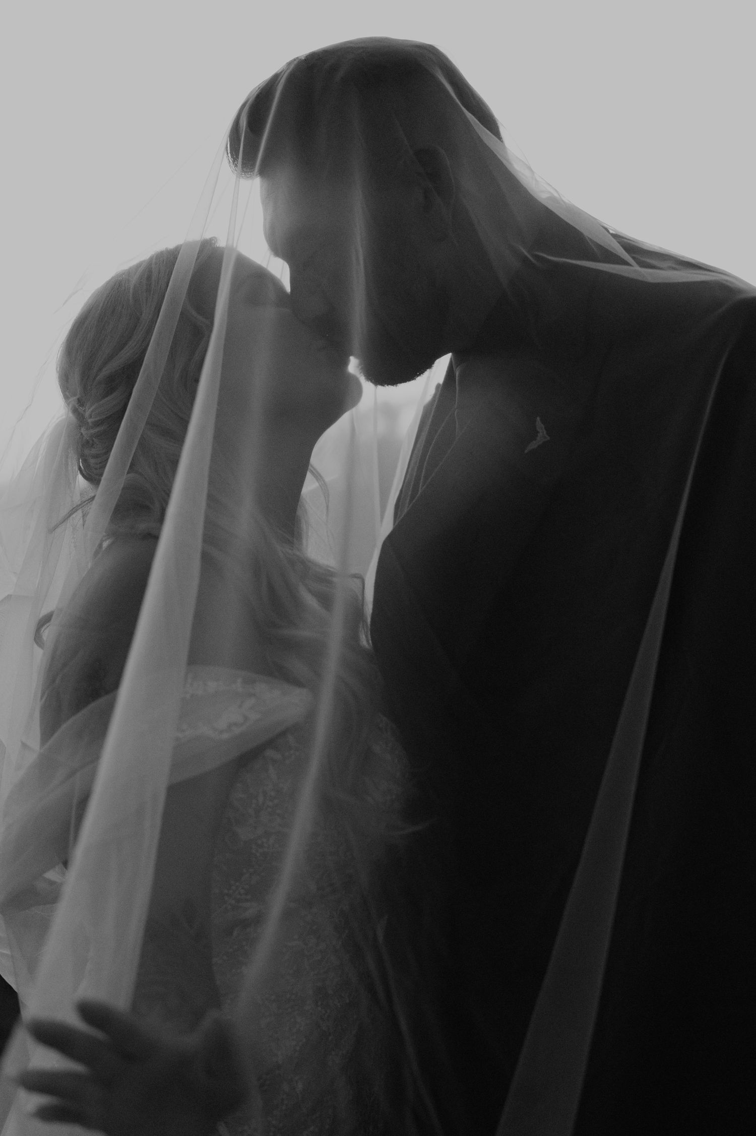 Artistic black and white silhouettes capture intimate wedding moments through a veil.