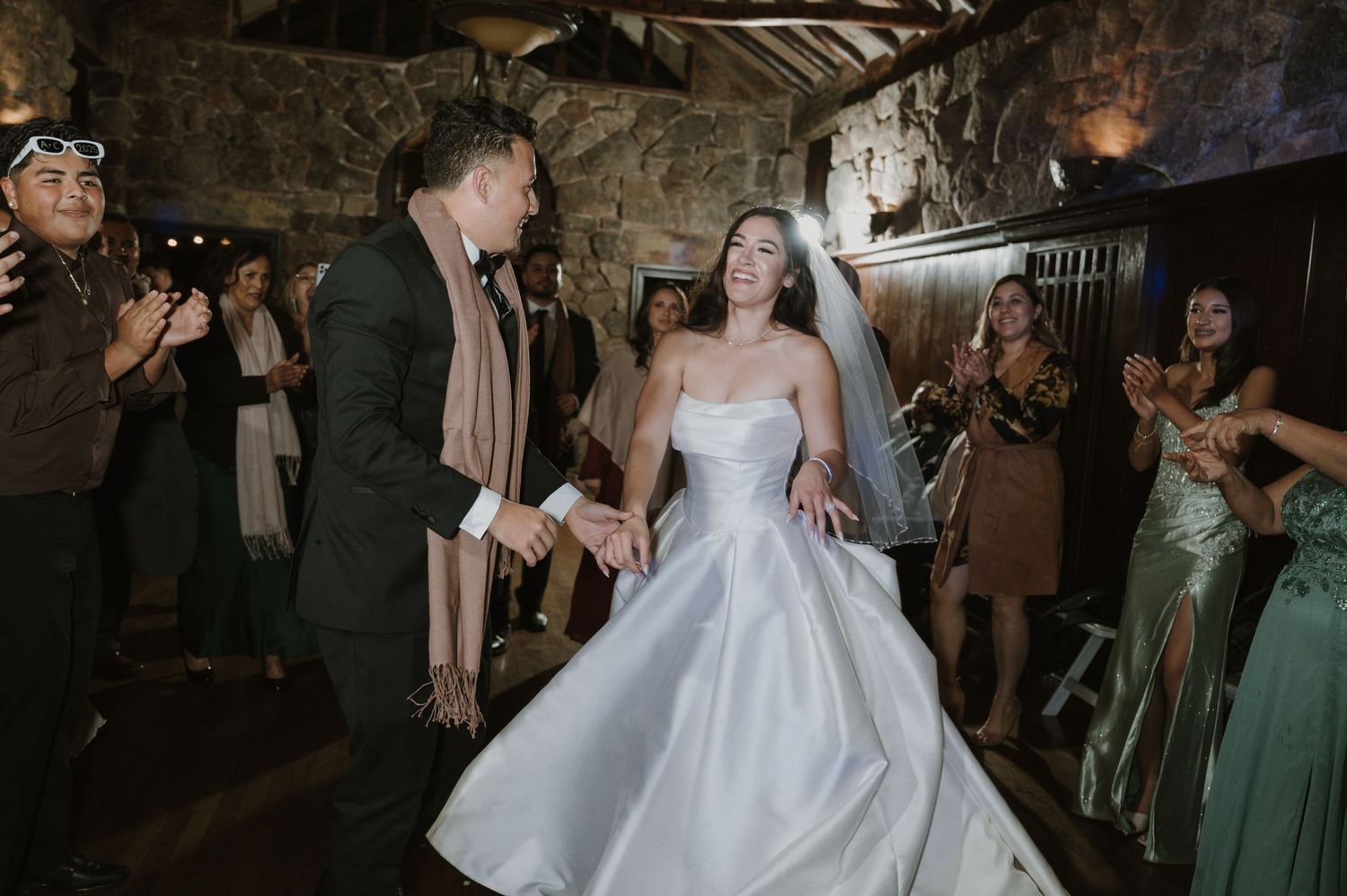Wedding guests dance joyfully at a rustic stone venue with twinkling lights overhead.