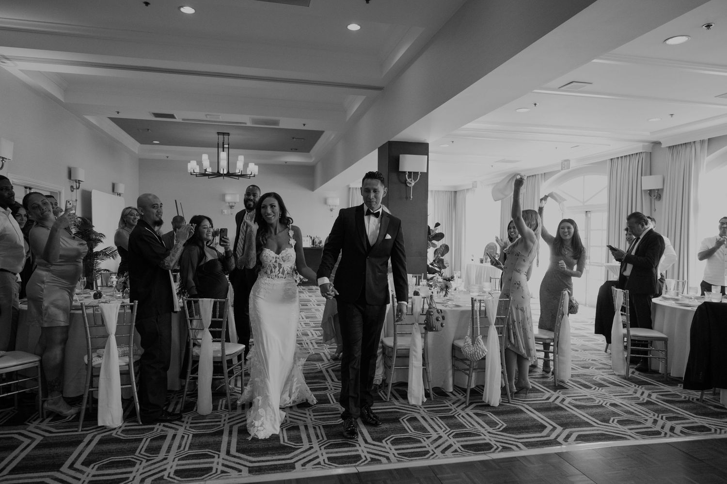 Wedding guests stand and cheer during a reception celebration in a ballroom.