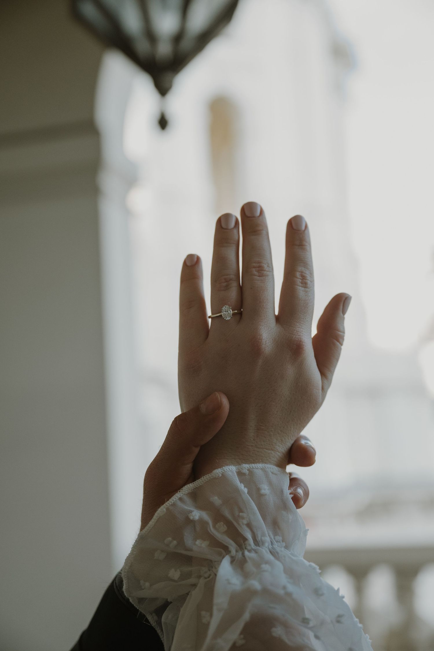 Close-up of hands with lace sleeves reaching upward against a bright window.