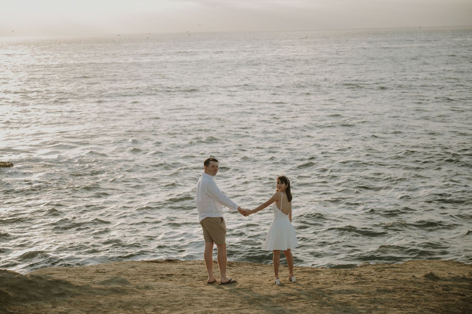 Couple standing on oceanside cliff with waves crashing below.