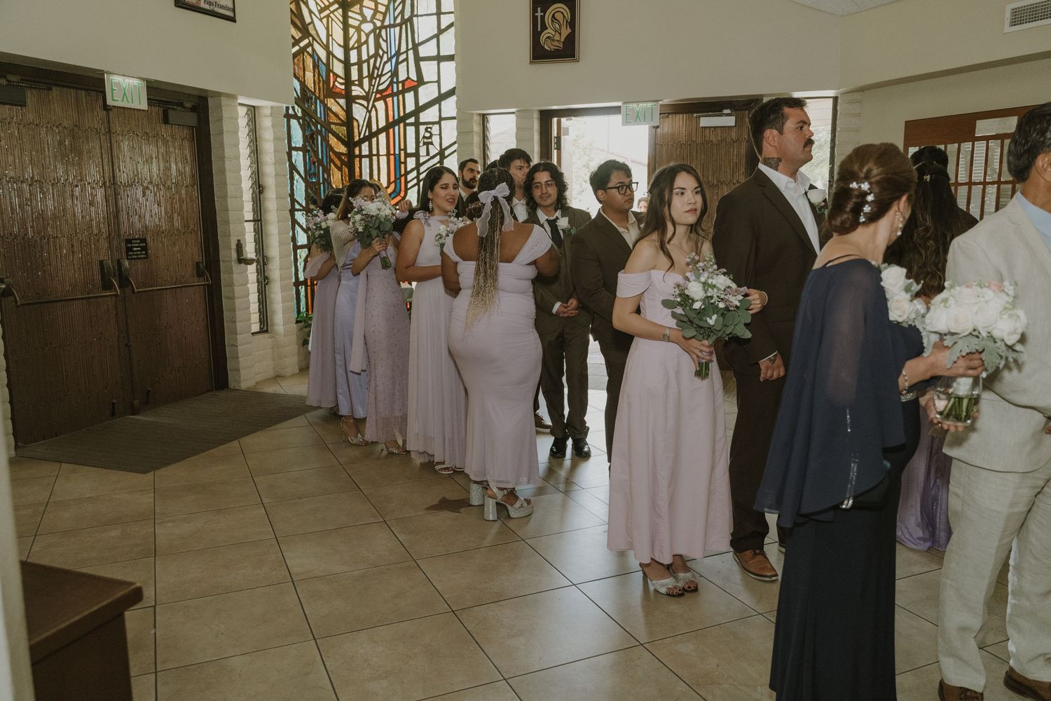 Bridesmaids in pink dresses line up inside a church before a wedding ceremony.