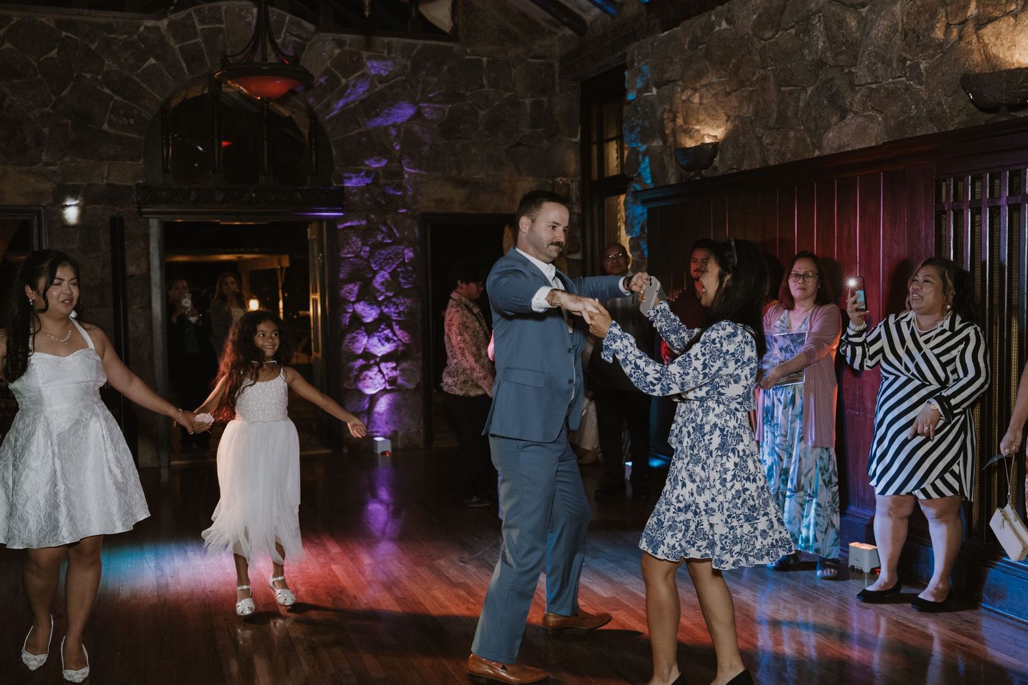 Wedding guests dancing joyfully on the dance floor at a rustic stone venue reception.