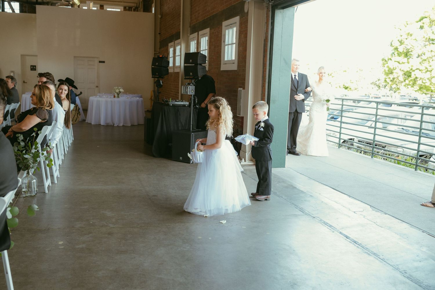 Flower girl and ring bearer walking down the aisle at an indoor wedding ceremony venue.