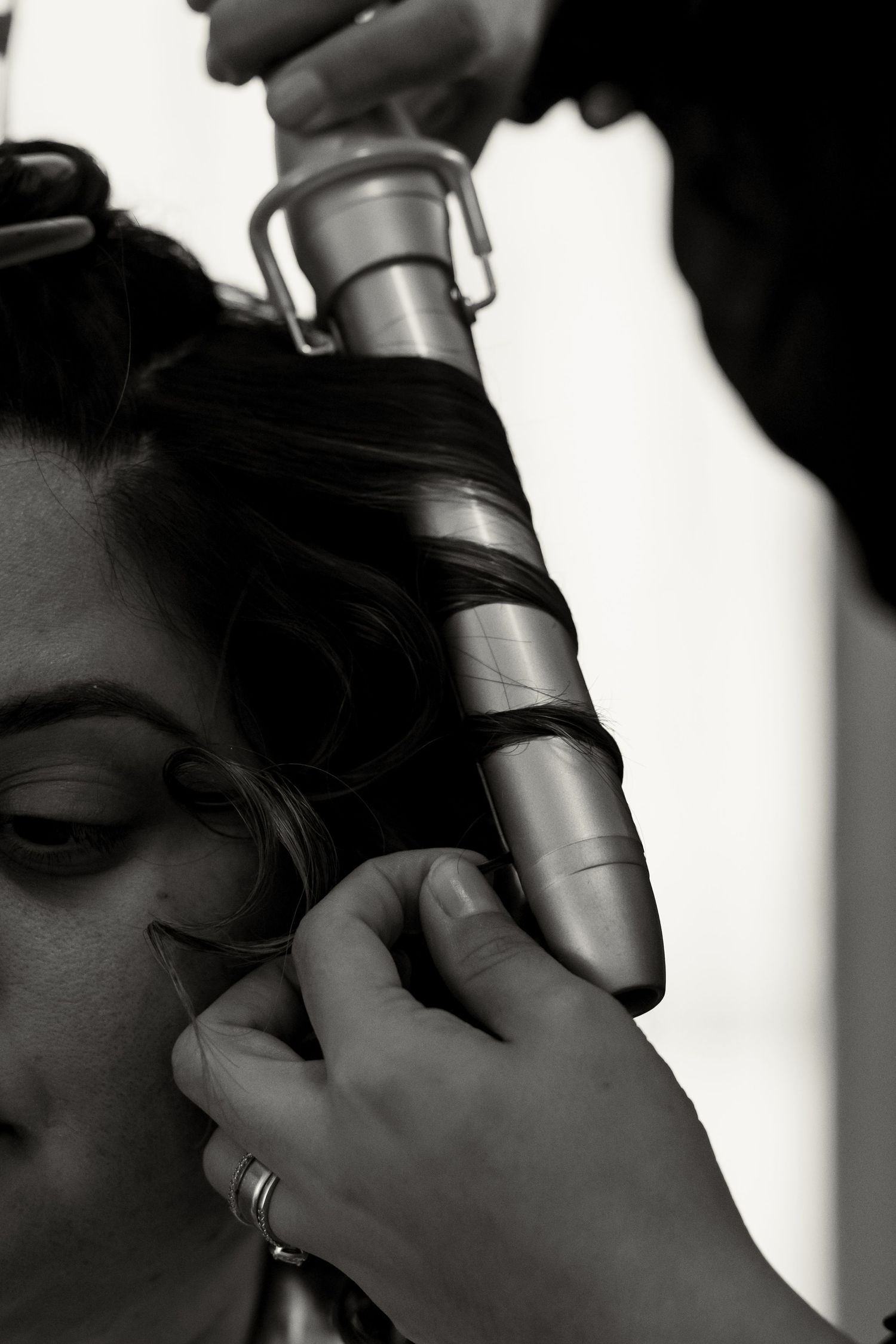 Black and white photo of a hairstylist curling a bride's dark hair with a large barrel curling iron.