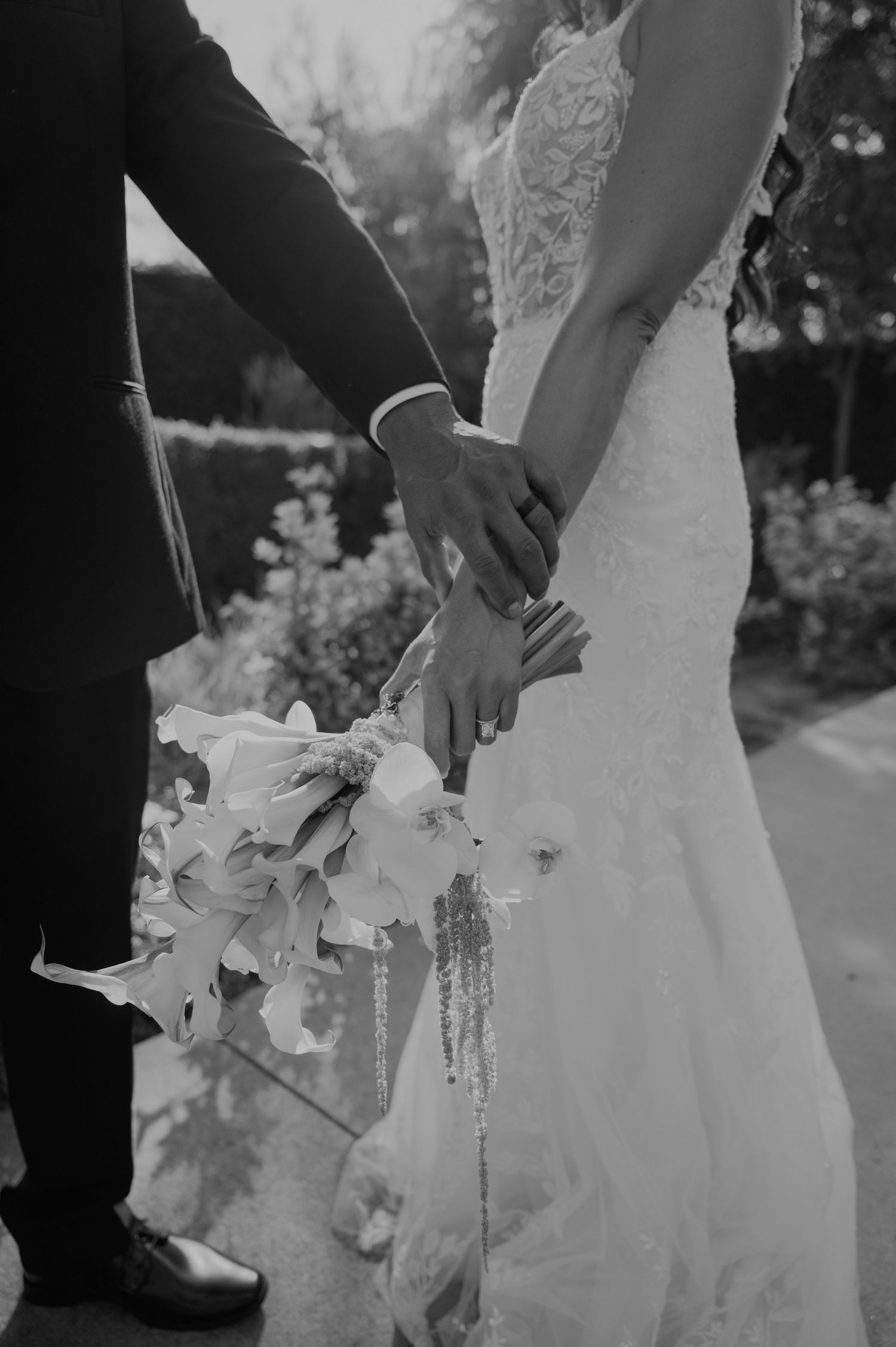 Bride and groom holding hands with white floral bouquet in black and white wedding photo.