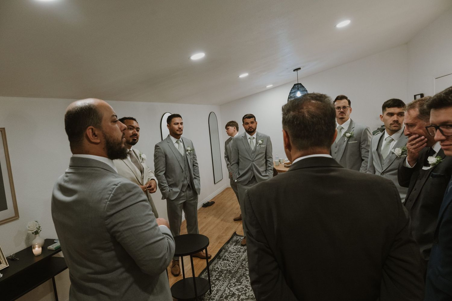 Groomsmen in matching gray suits standing together in a bright white room before a wedding ceremony.