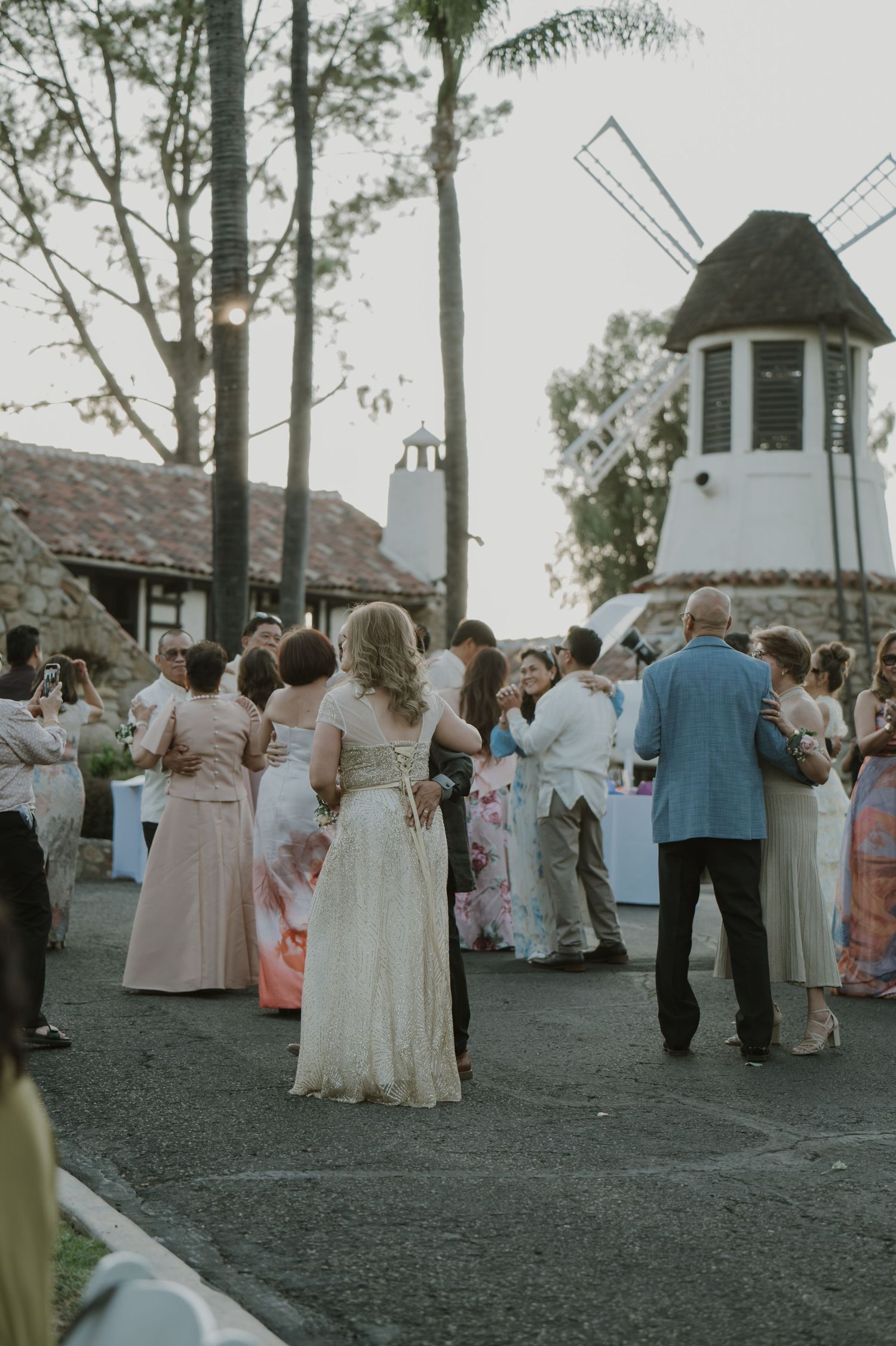Wedding guests dancing outdoors near a white windmill at a garden reception venue at dusk.