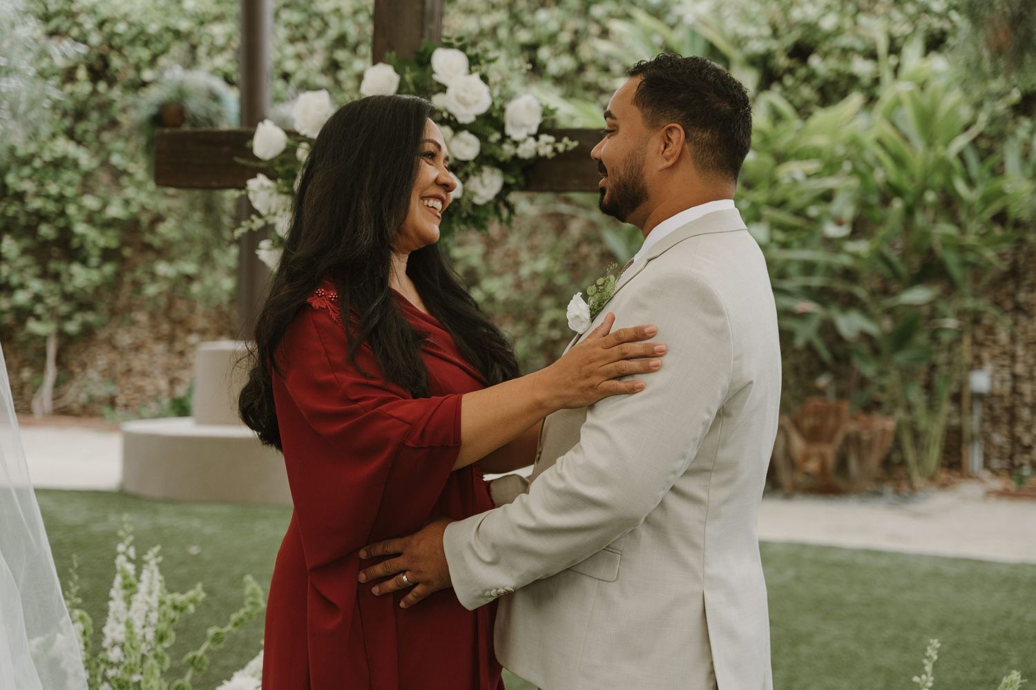 Couple sharing a romantic moment at outdoor wedding ceremony, bride in red dress and groom in white suit.
