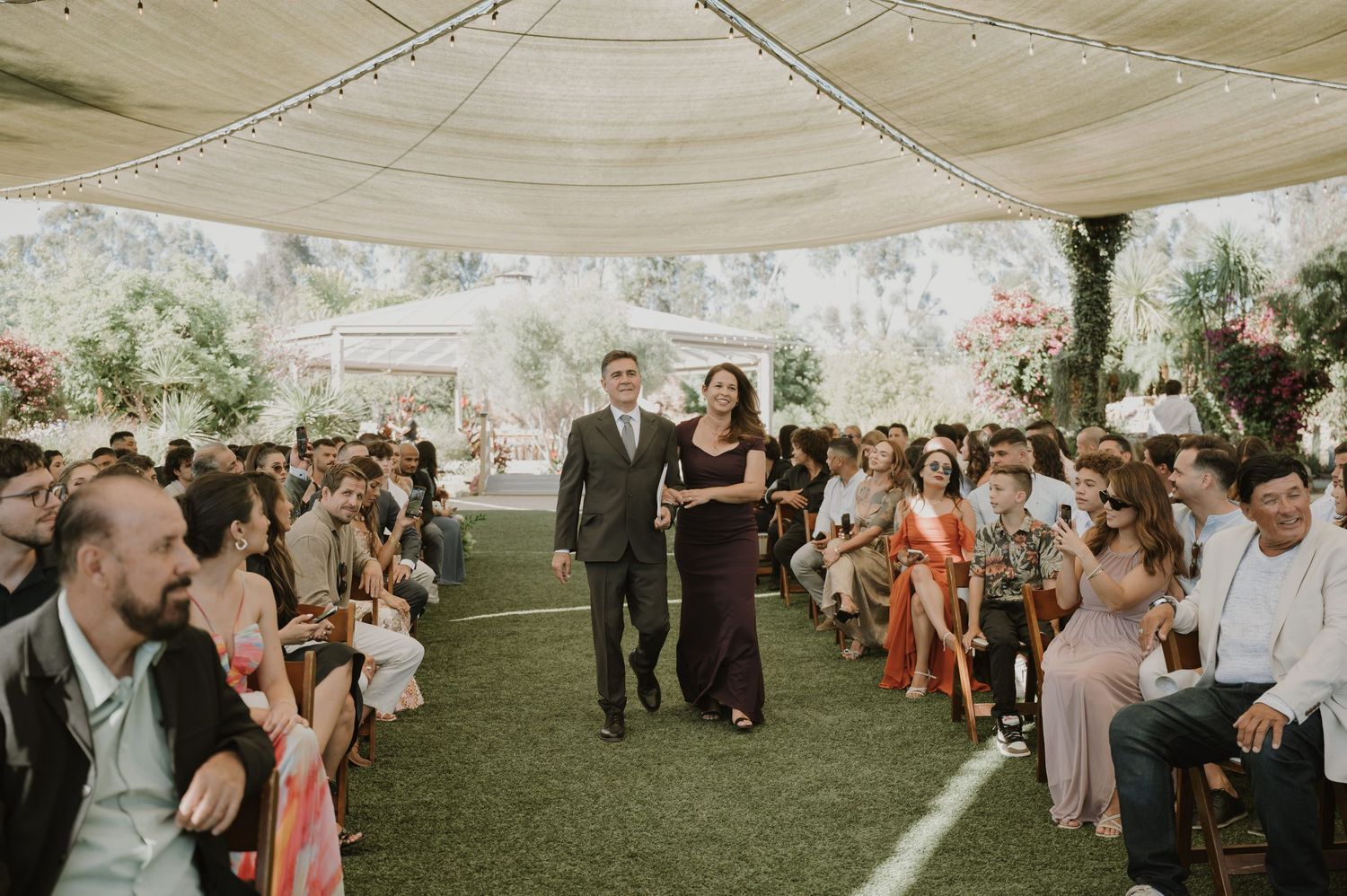 Couple walks down the aisle at an outdoor wedding ceremony under a tent with seated guests.