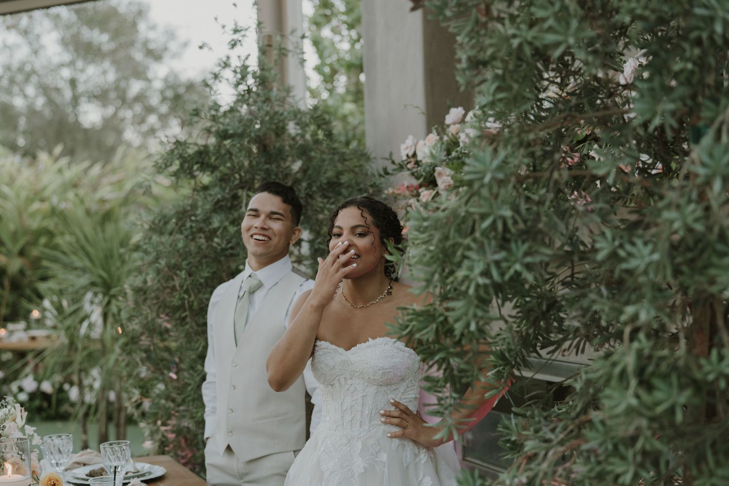 Bride and groom smile joyfully outdoors surrounded by lush greenery at their elegant garden wedding ceremony.