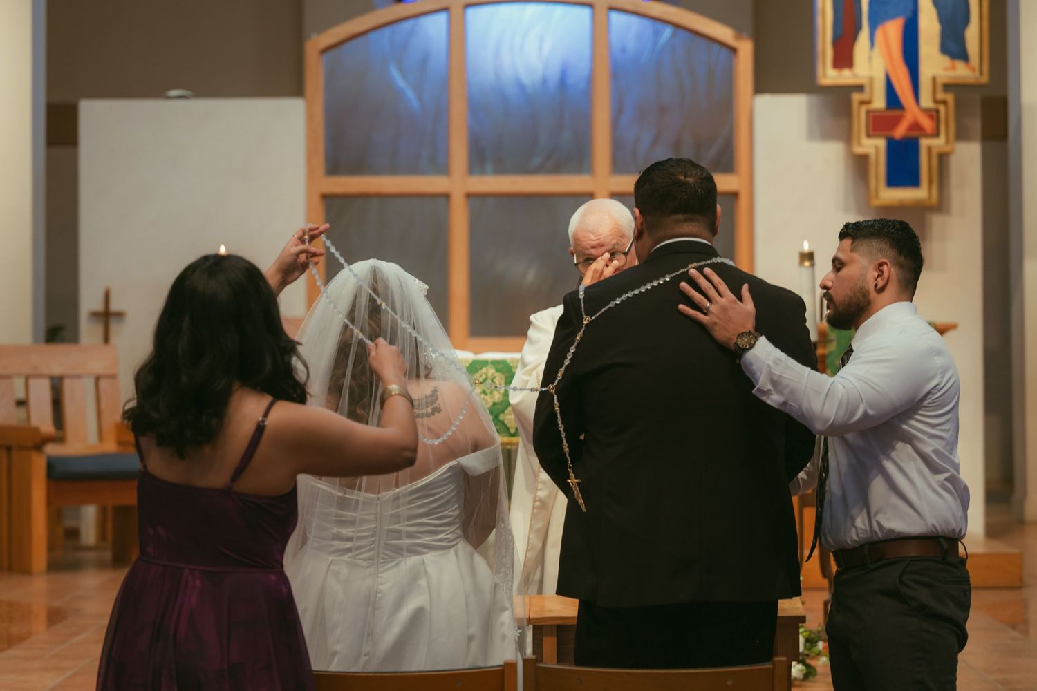 Wedding ceremony in church with bride in veil, groom, officiant, and attendants gathered at the altar.