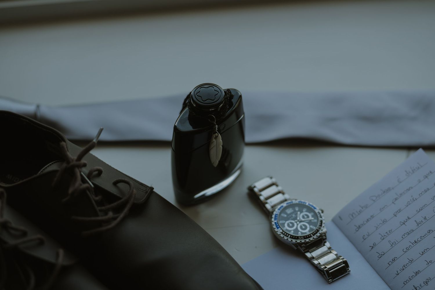 Elegant men's accessories arranged on a surface, featuring a luxury chronograph watch, cologne bottle, dress shoes, and tie.