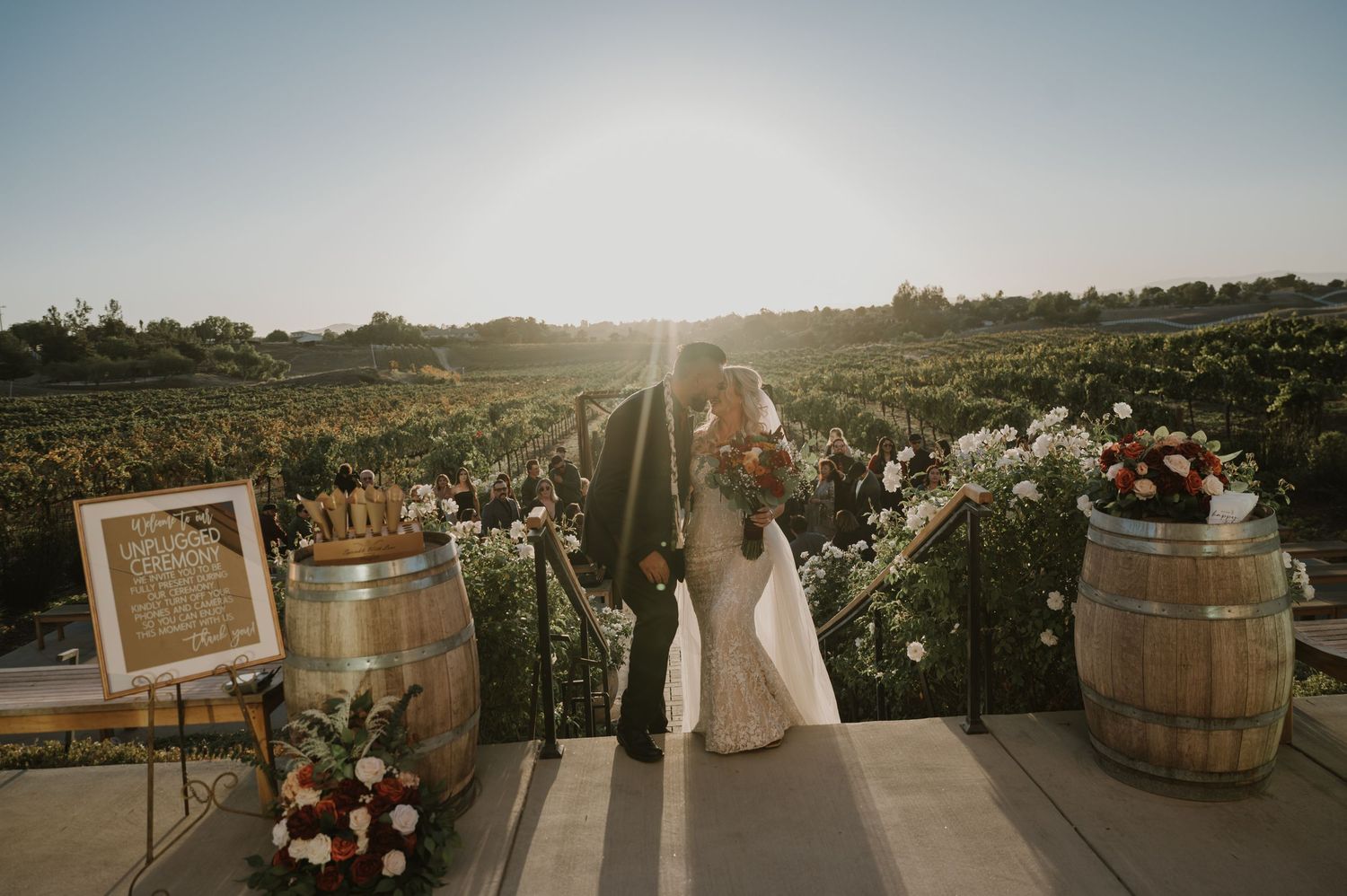 Wedding ceremony setup at a winery with decorative barrels and floral arrangements.