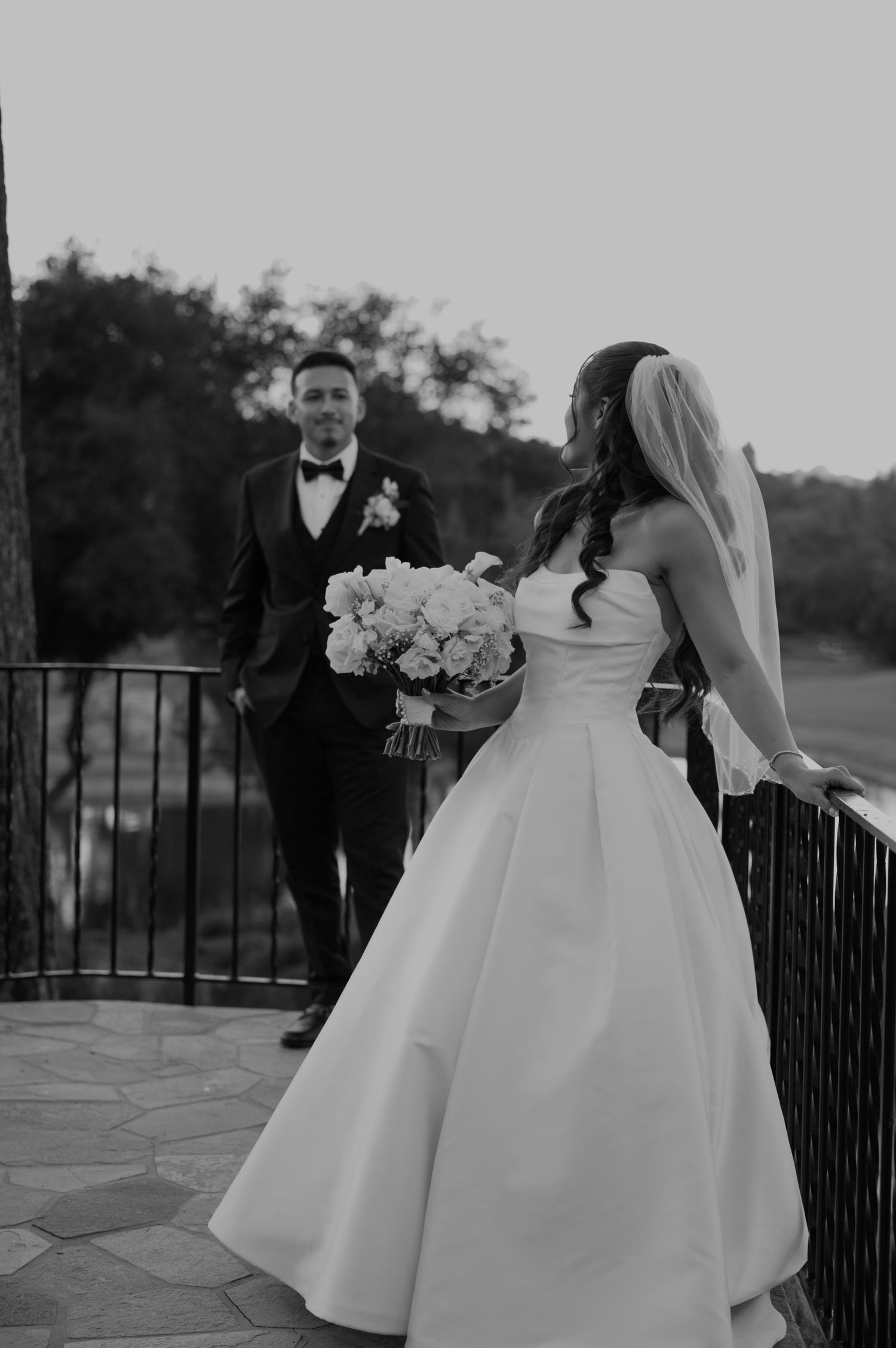 Black and white wedding photo of couple on stone patio with bride holding white floral bouquet.