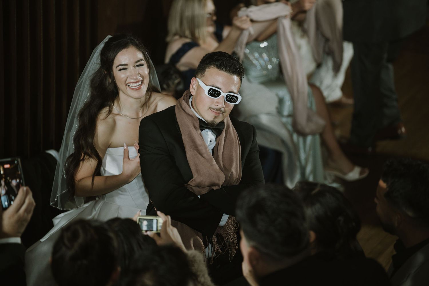 Wedding guests dance and celebrate with sunglasses and formal attire at nighttime reception.