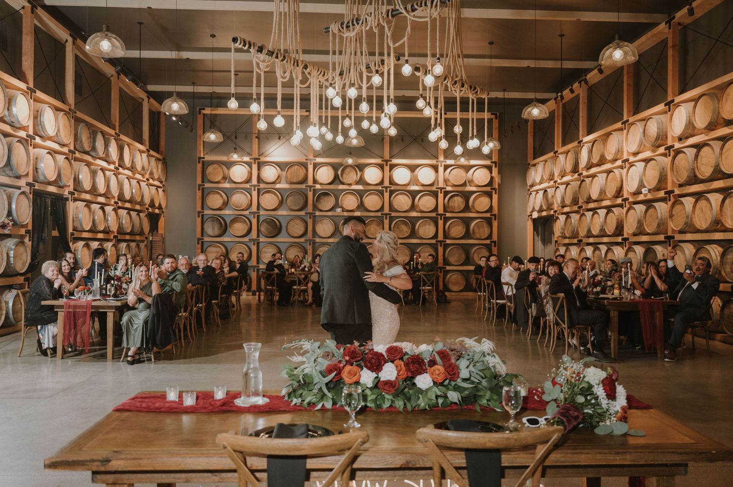 Rustic winery barrel room decorated with warm lighting and floral arrangements for an elegant event.