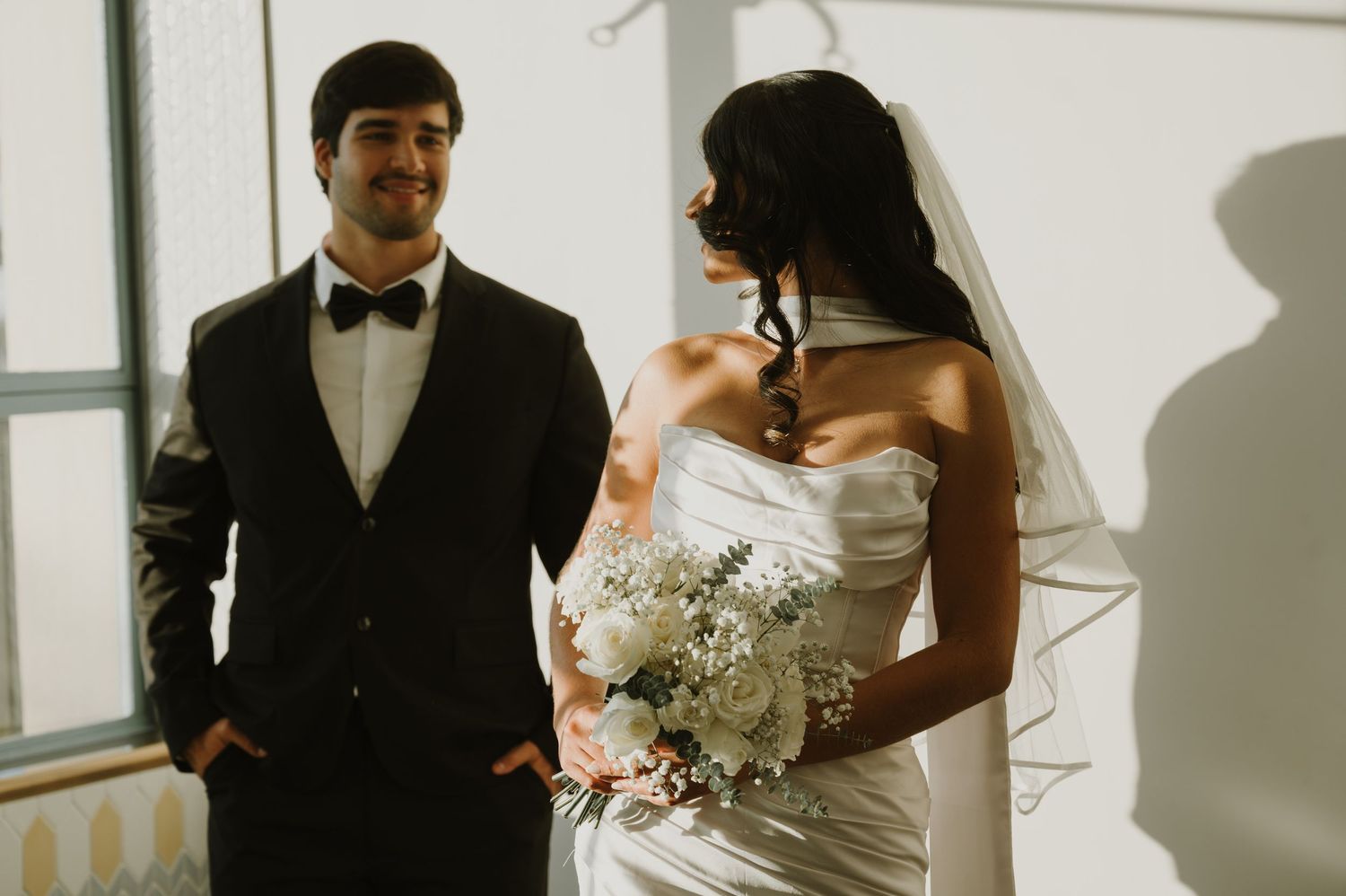 Bride in white dress and groom in black suit share an intimate moment during their wedding photoshoot.