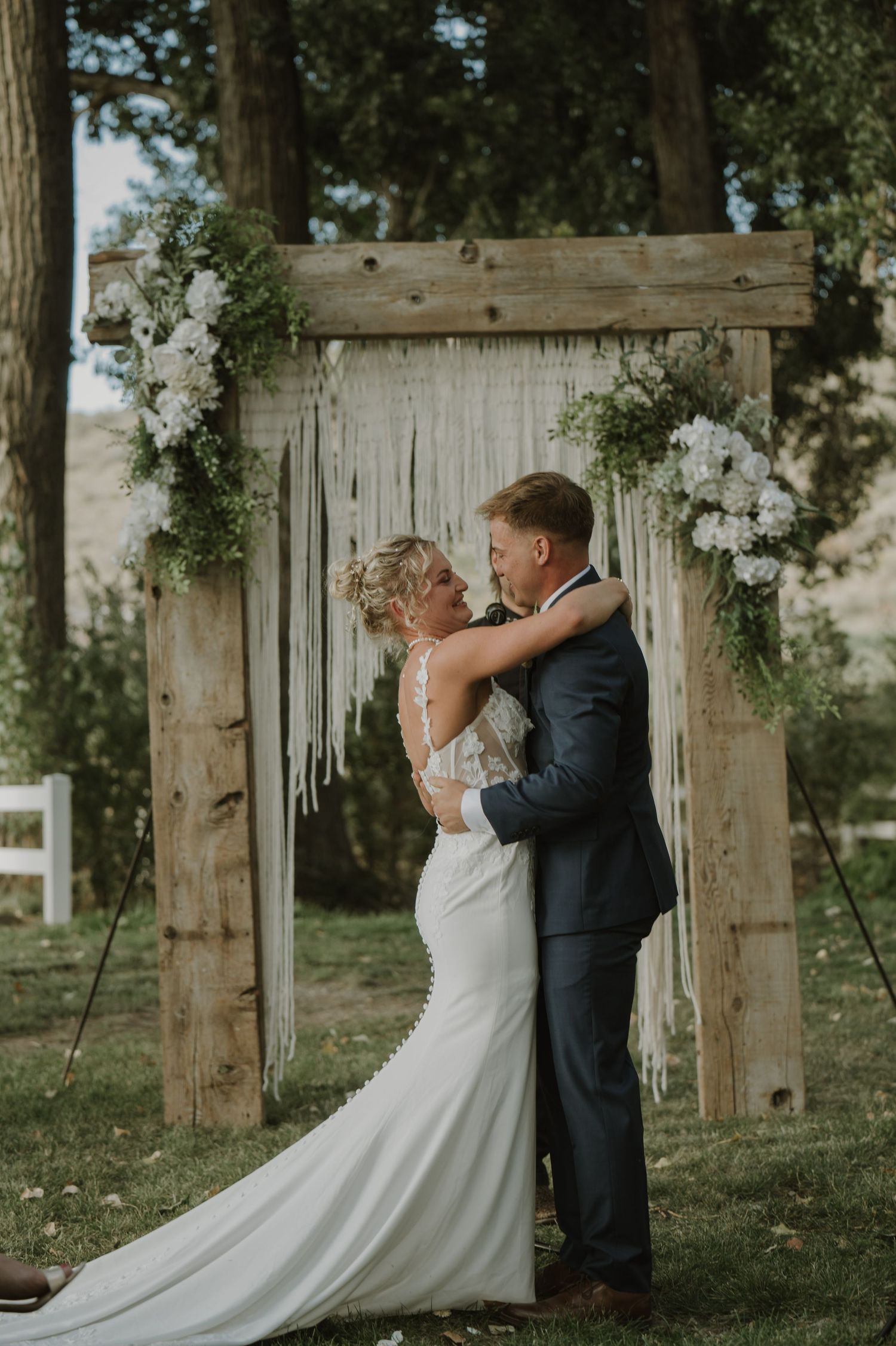 A couple shares their first dance in front of a rustic wooden backdrop decorated with white flowers.