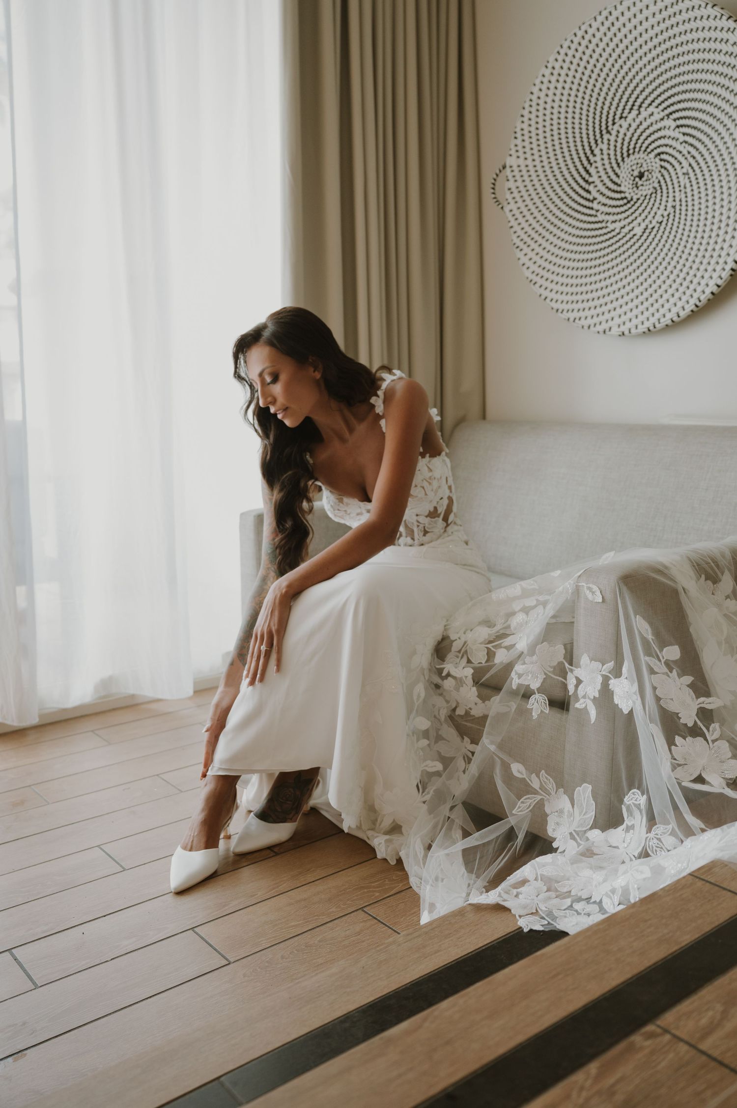 Wedding dress detail with flowing fabric against wooden flooring in a bright room.