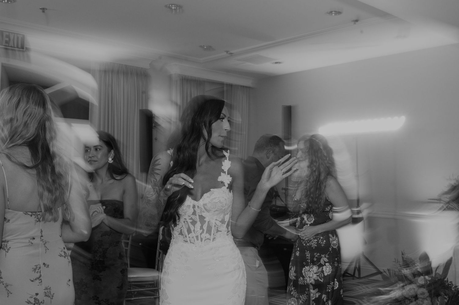 Wedding guests dance and celebrate together on a wooden dance floor at an indoor reception venue.