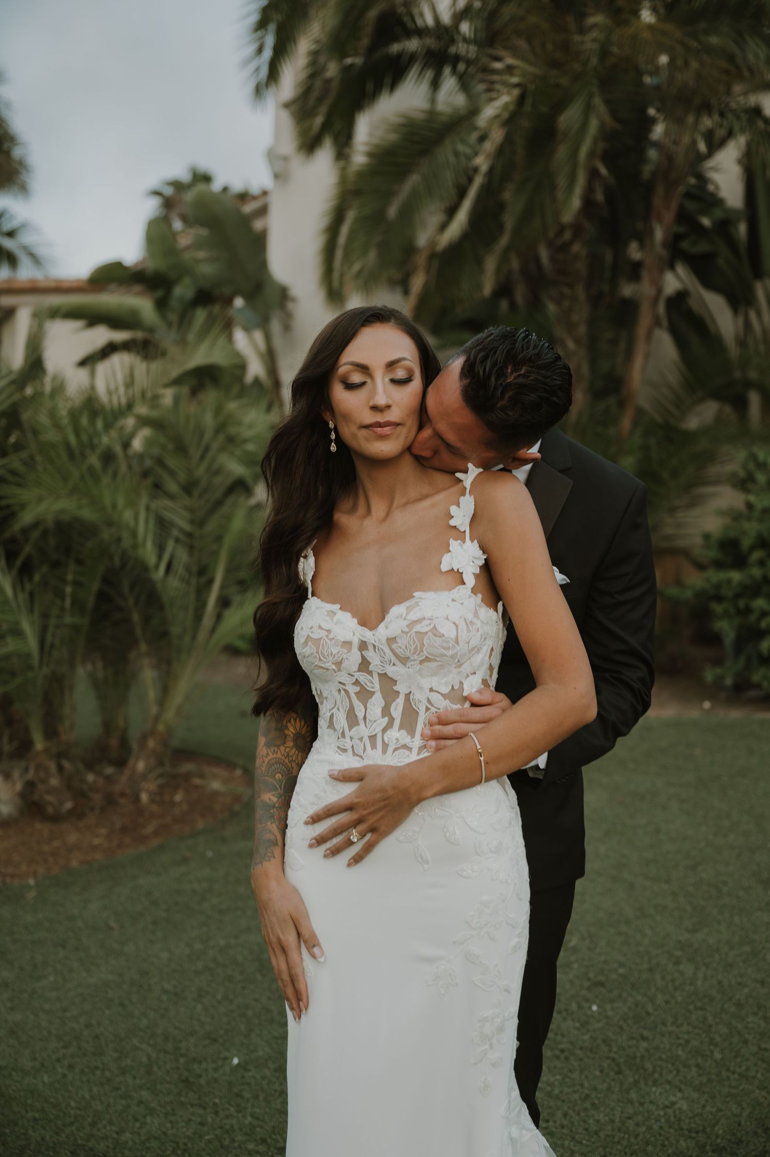A romantic wedding portrait in a tropical garden setting with palm trees.