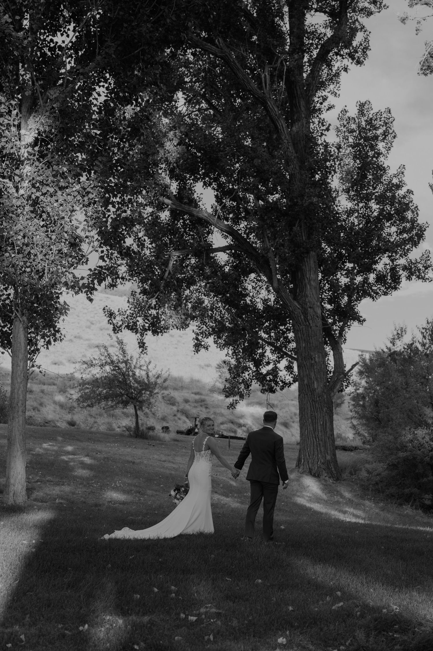 A black and white wedding photo showing a couple walking through a scenic hillside landscape.